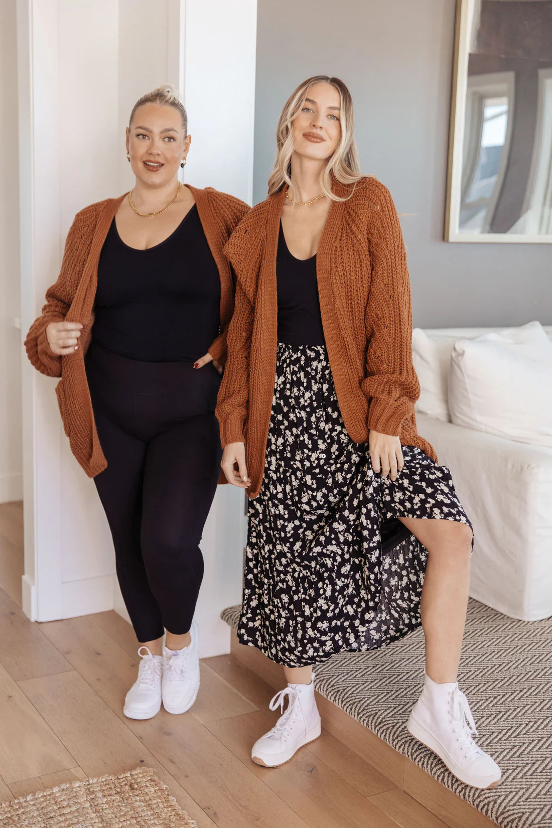 Two women wearing chestnut knit cardigans styled with black tops, leggings, and a floral skirt in a cozy indoor setting