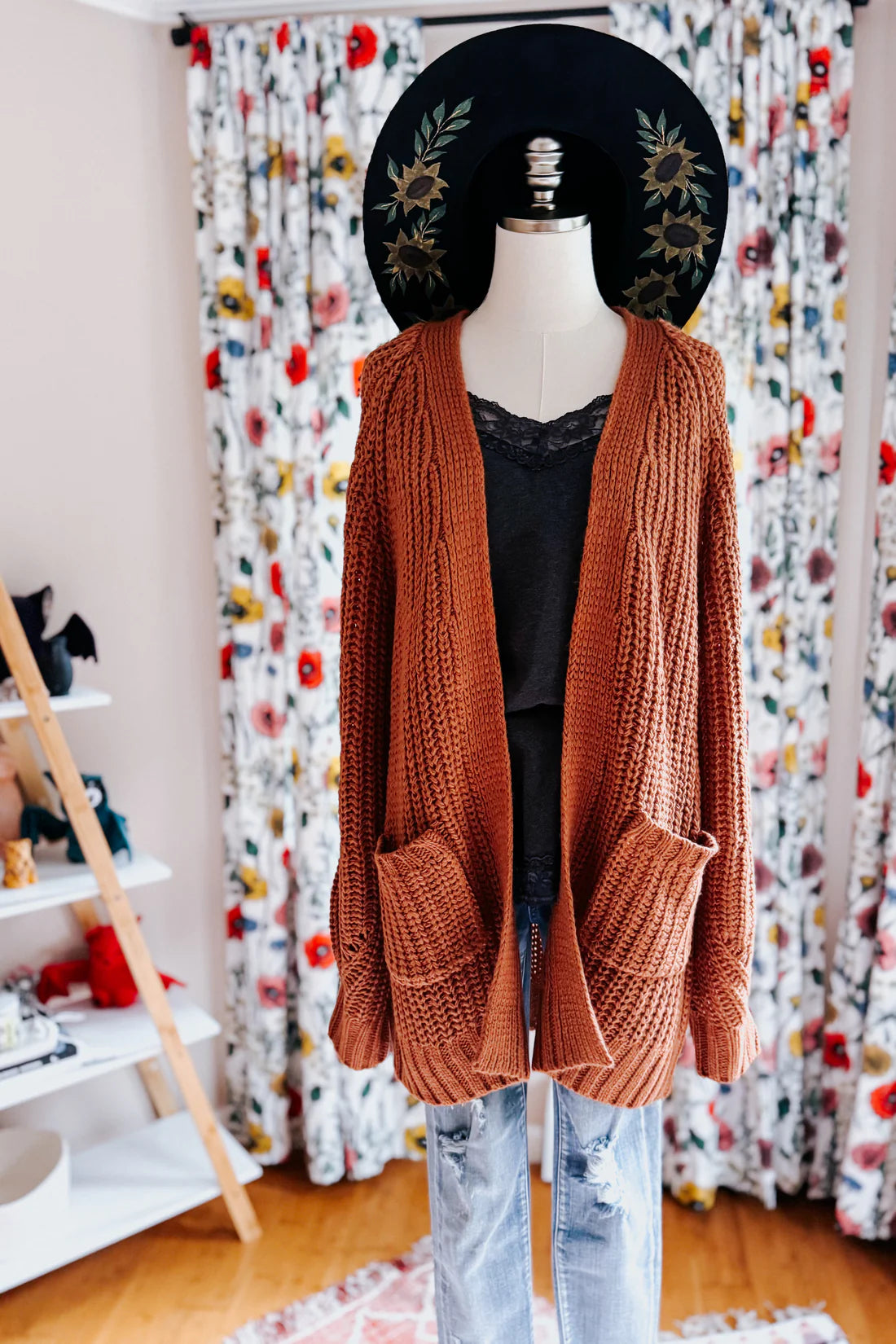 Chestnut knit cardigan with textured stitch and large pockets layered over black lace top and distressed jeans on mannequin