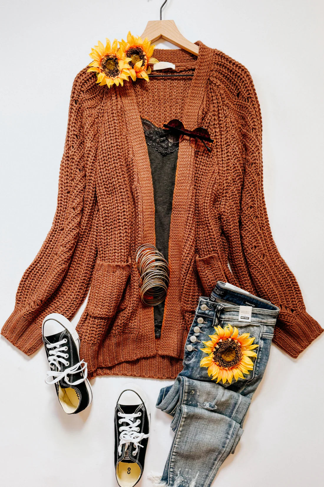 Chestnut chunky knit cardigan with large pockets styled with black lace top, distressed jeans, sneakers, and sunflowers flat lay
