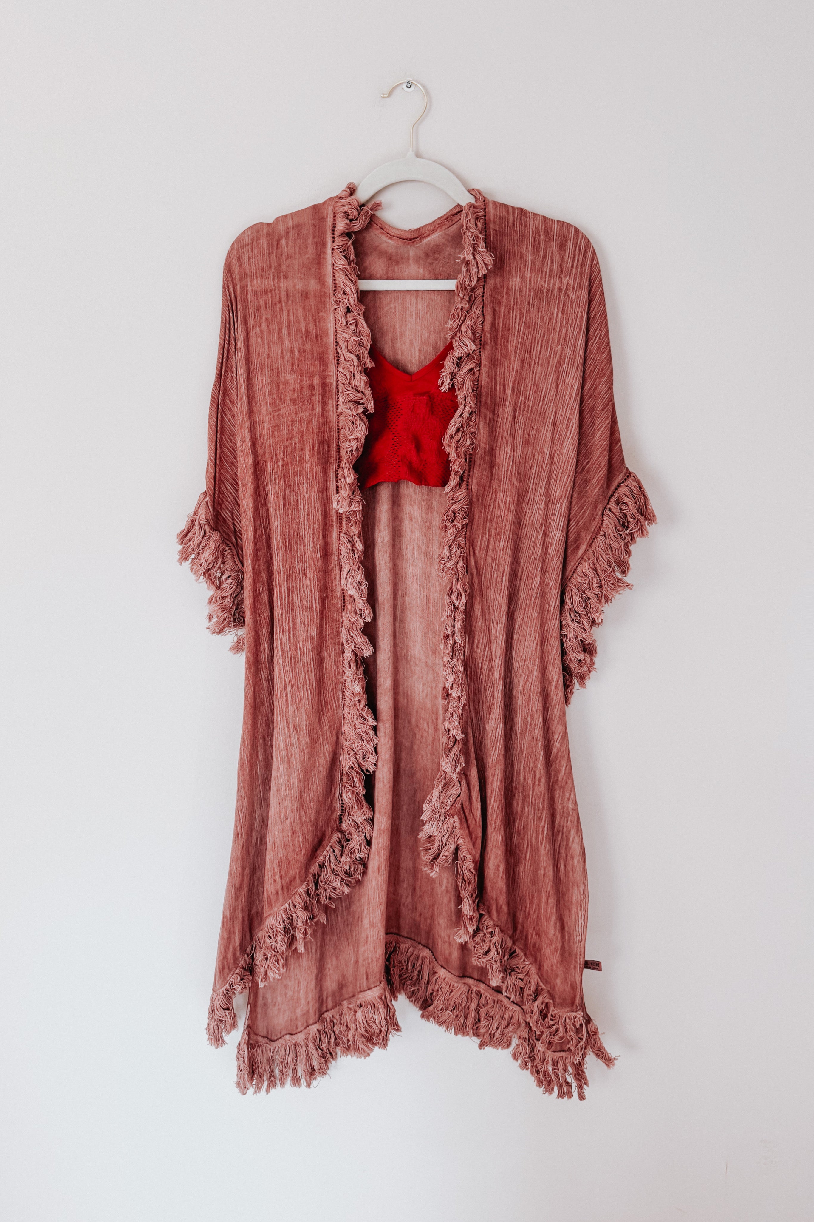 Rose-colored plush duster with sunbleached texture and fringe edges hanging on a white wall hanger