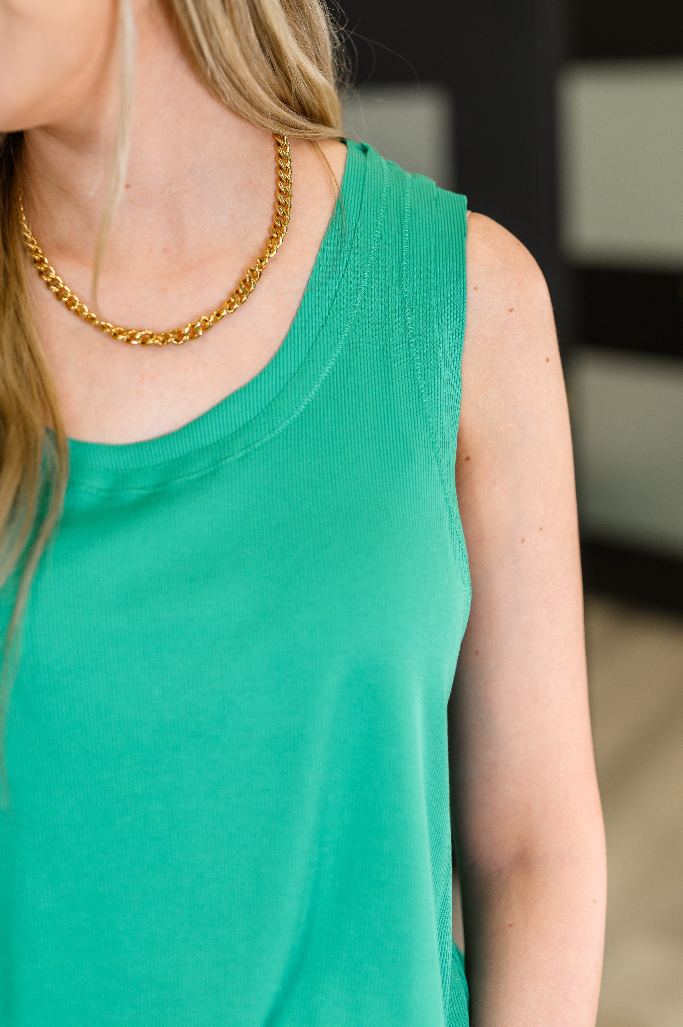 Close-up of relaxed green knit tank worn with gold chain necklace on woman with blonde hair indoors