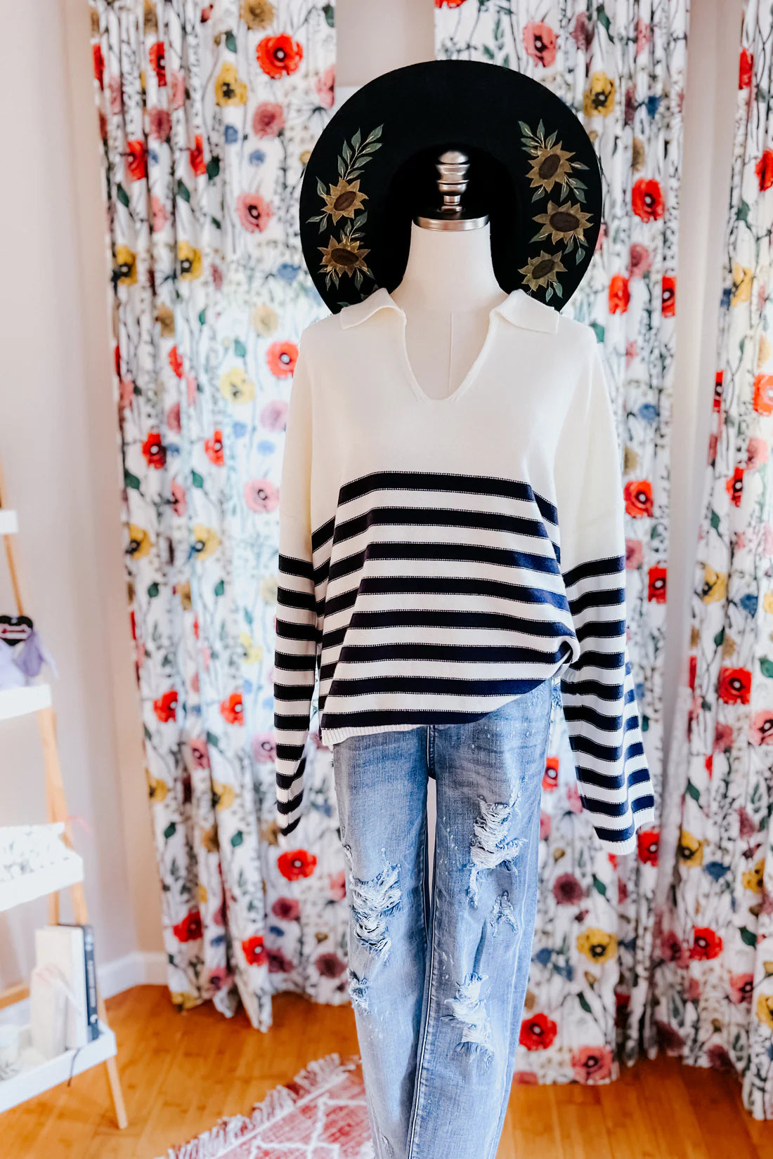 White sweater featuring navy horizontal stripes on the lower half and sleeves, styled with distressed light wash jeans on a mannequin.