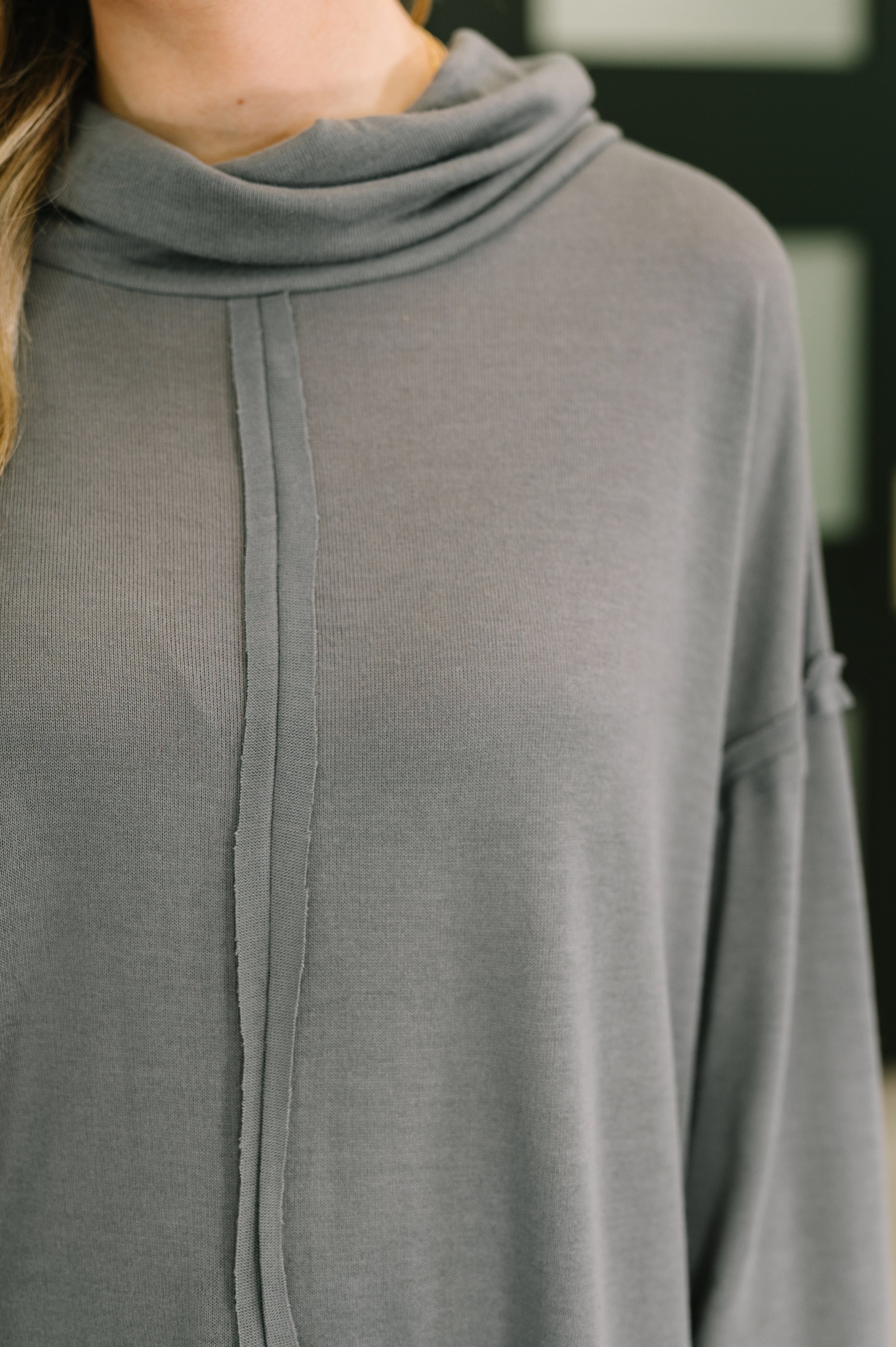 Close-up of a grey turtleneck featuring a relaxed fit and a centered seam detail on soft fabric worn indoors.