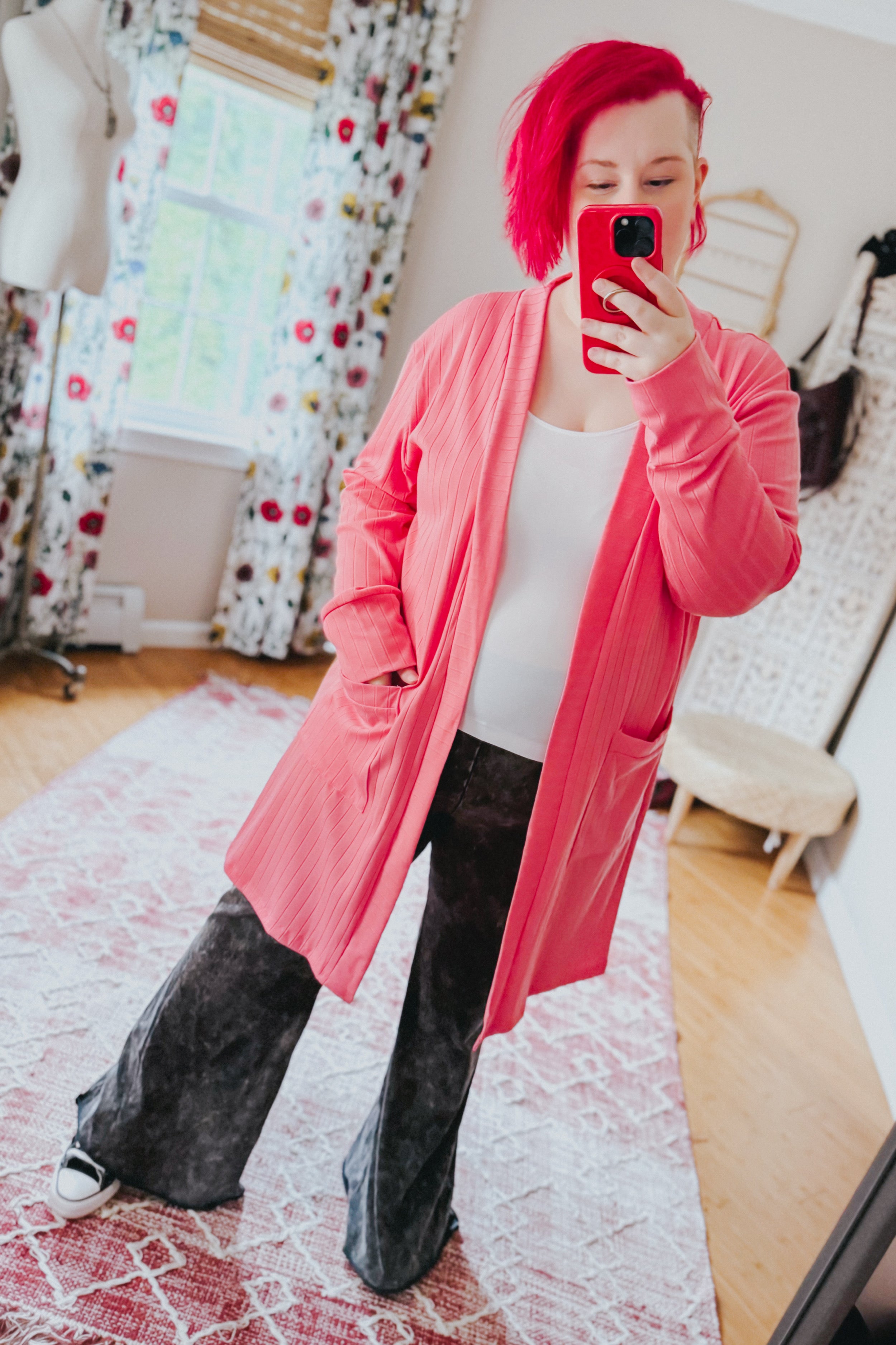 Woman taking mirror selfie wearing coral Modern Idealist open front cardigan with pockets over white top and black wide pants indoors