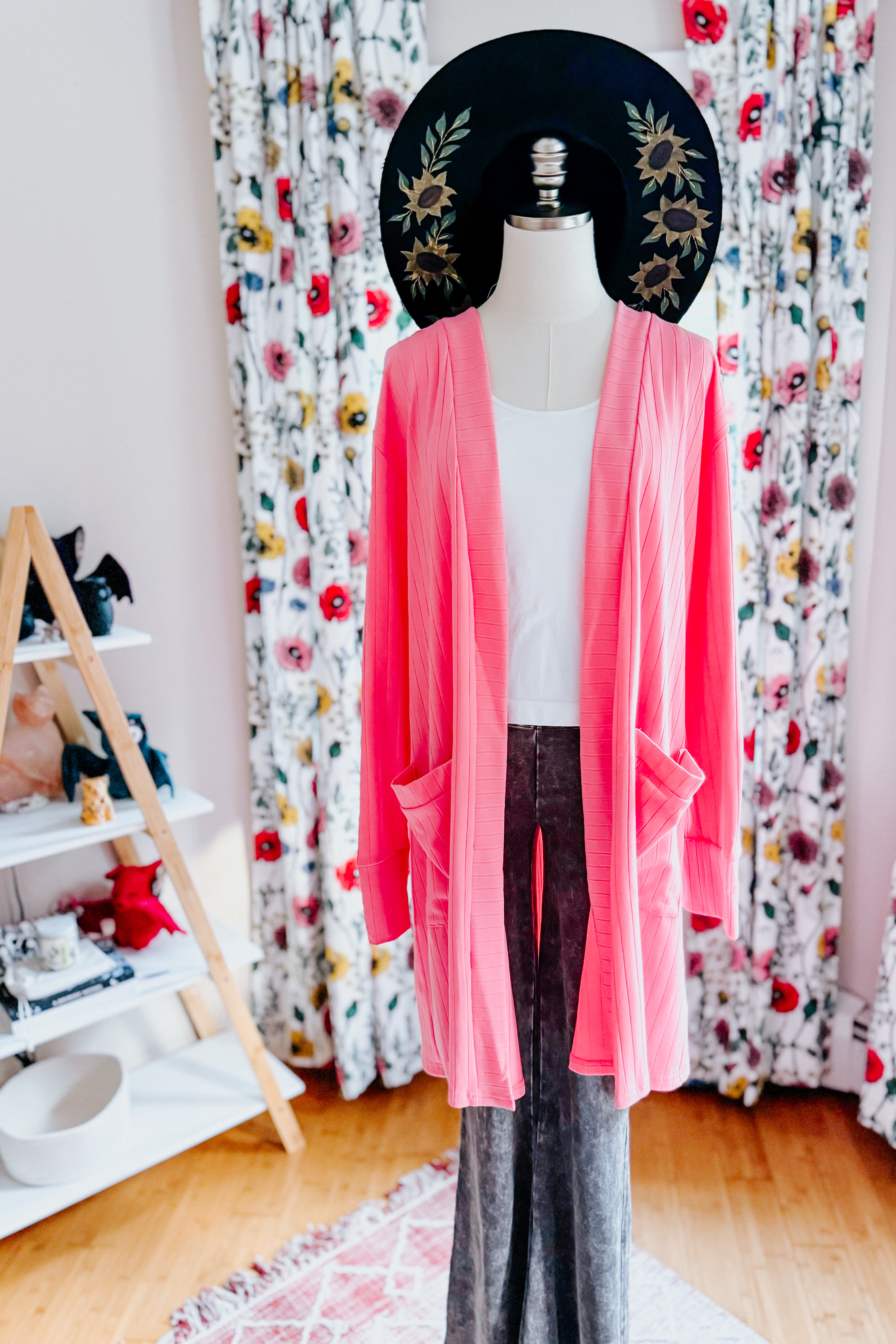 Bright coral Modern Idealist open front cardigan with pockets displayed on mannequin against floral curtains and wooden floor
