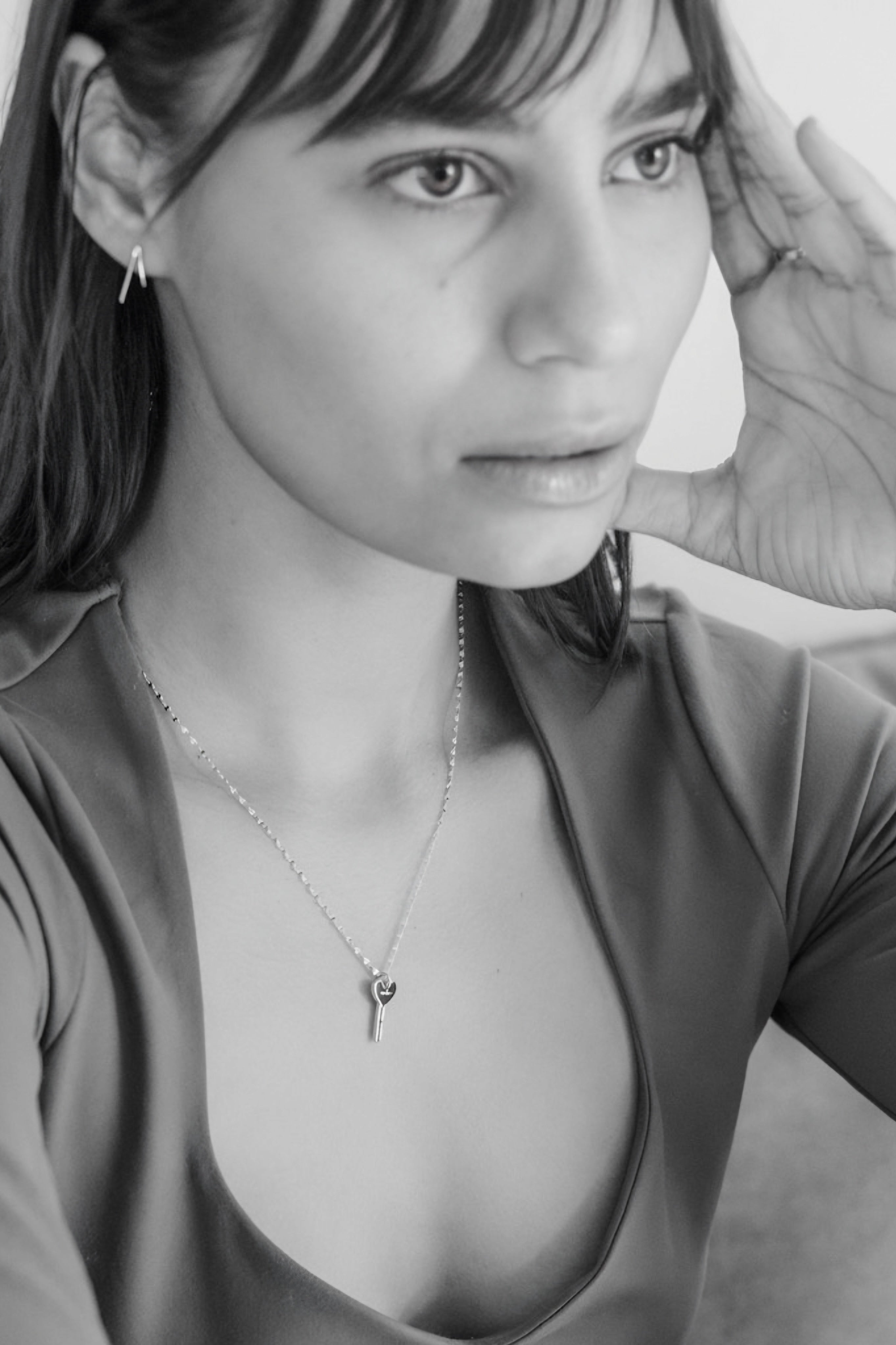 Close-up of a woman wearing a delicate silver key pendant necklace with a heart-shaped cutout, paired with a scoop-neck top.