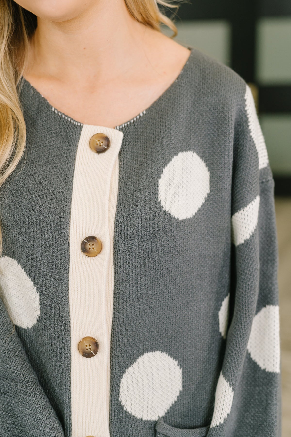 Close-up of a woman wearing a charcoal knit cardigan with cream button placket trim and oversized polka dots