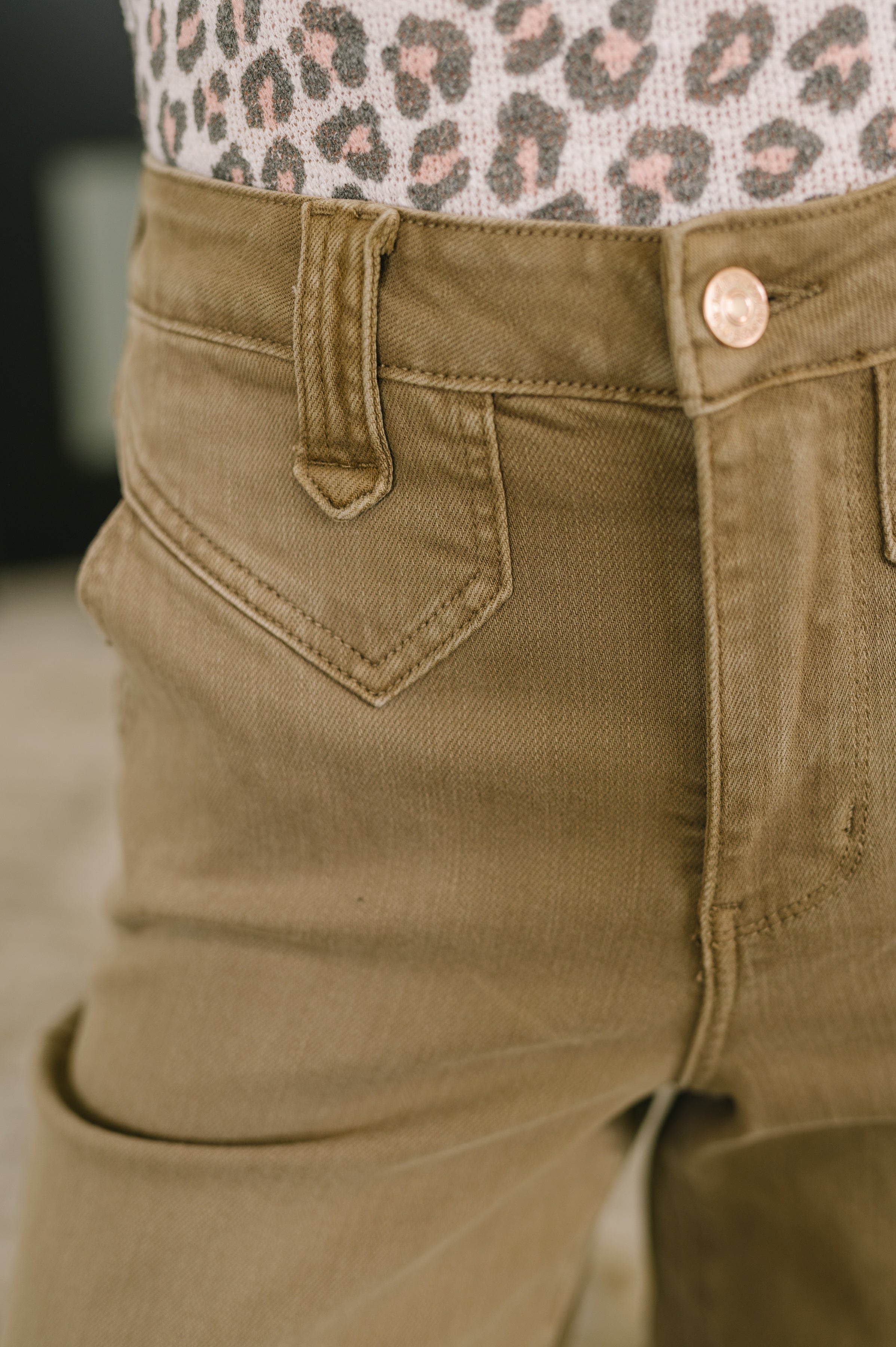 Close-up of brown high-rise wide-leg ankle jeans showcasing vintage front yoke and copper button detail with leopard print top