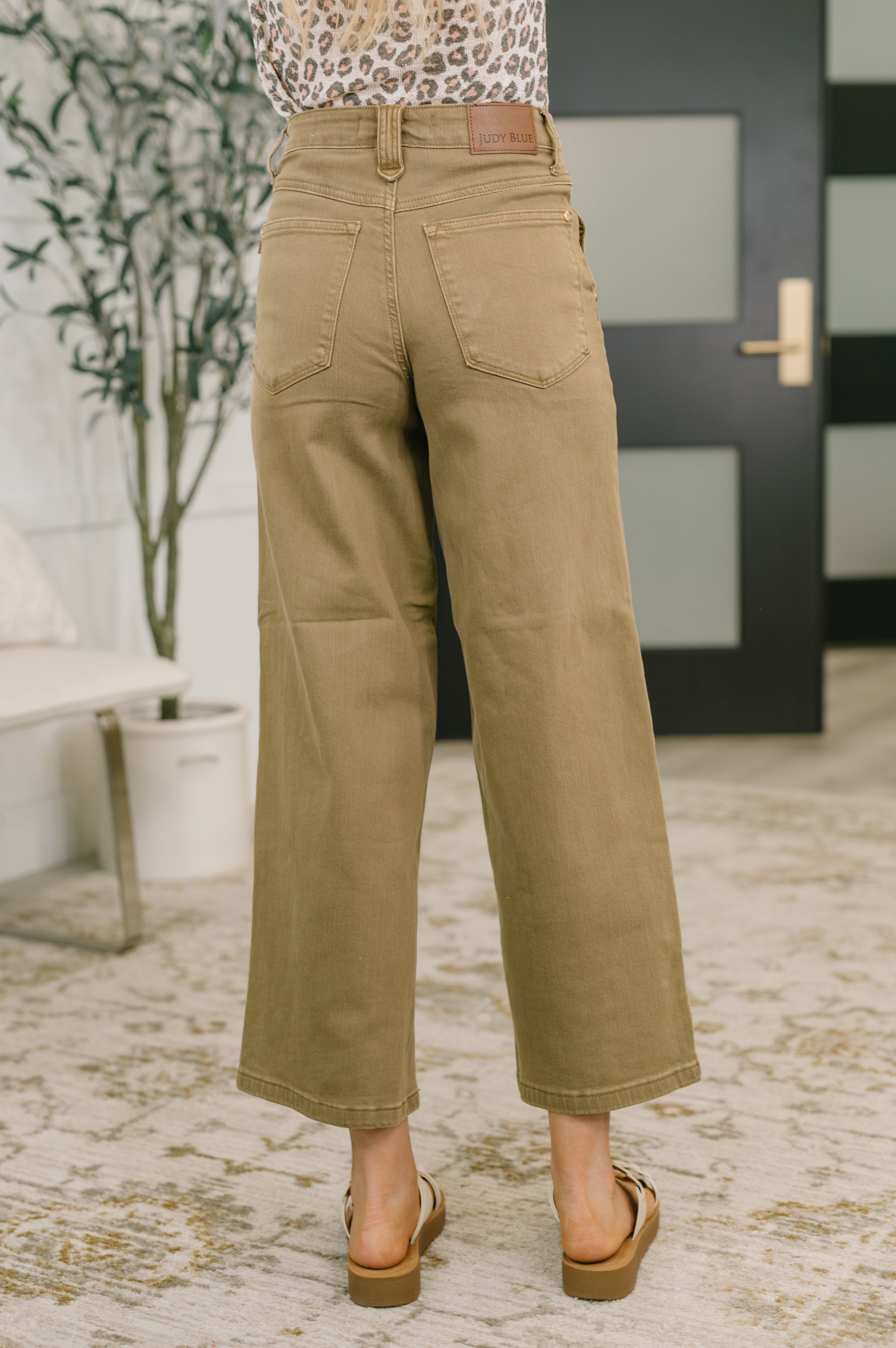 Back view of woman wearing brown high-waist wide-leg ankle jeans with vintage yoke and white sandals indoors