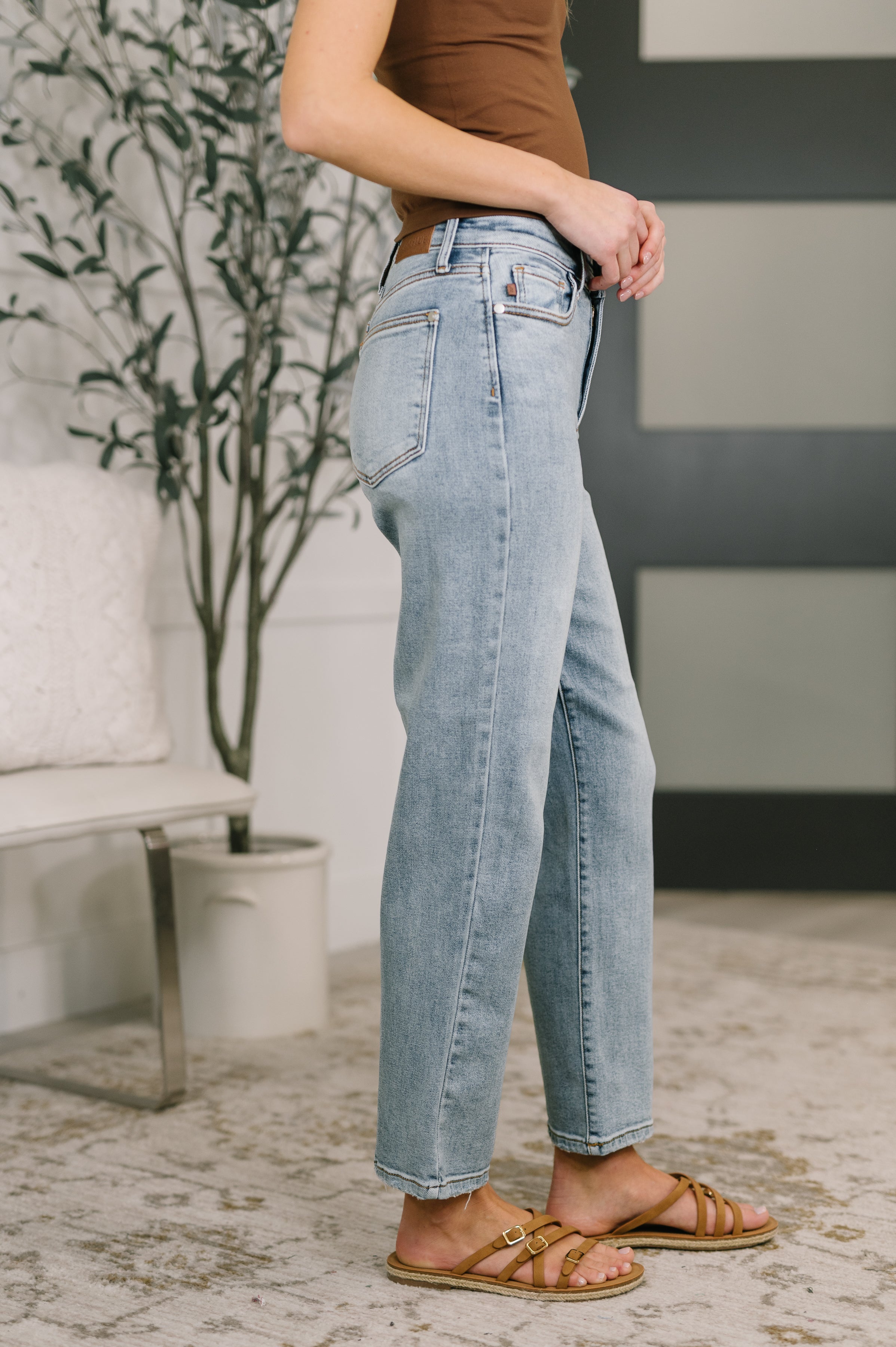 Side view of woman wearing blue Natalie High Waist Ankle Straight Jeans with slip-on sandals indoors