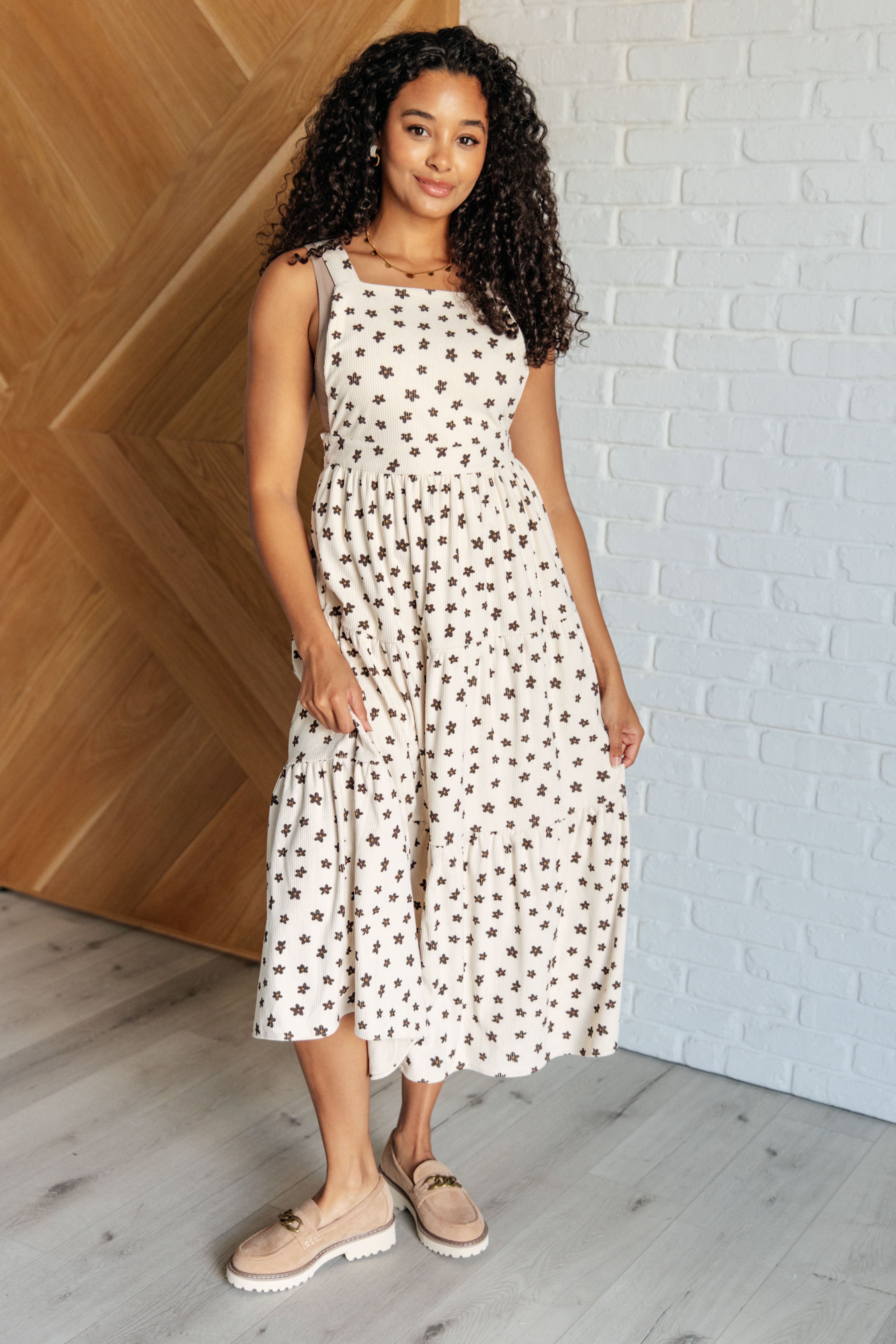 Woman wearing a cream sleeveless dress with a black floral pattern and tiered skirt standing indoors