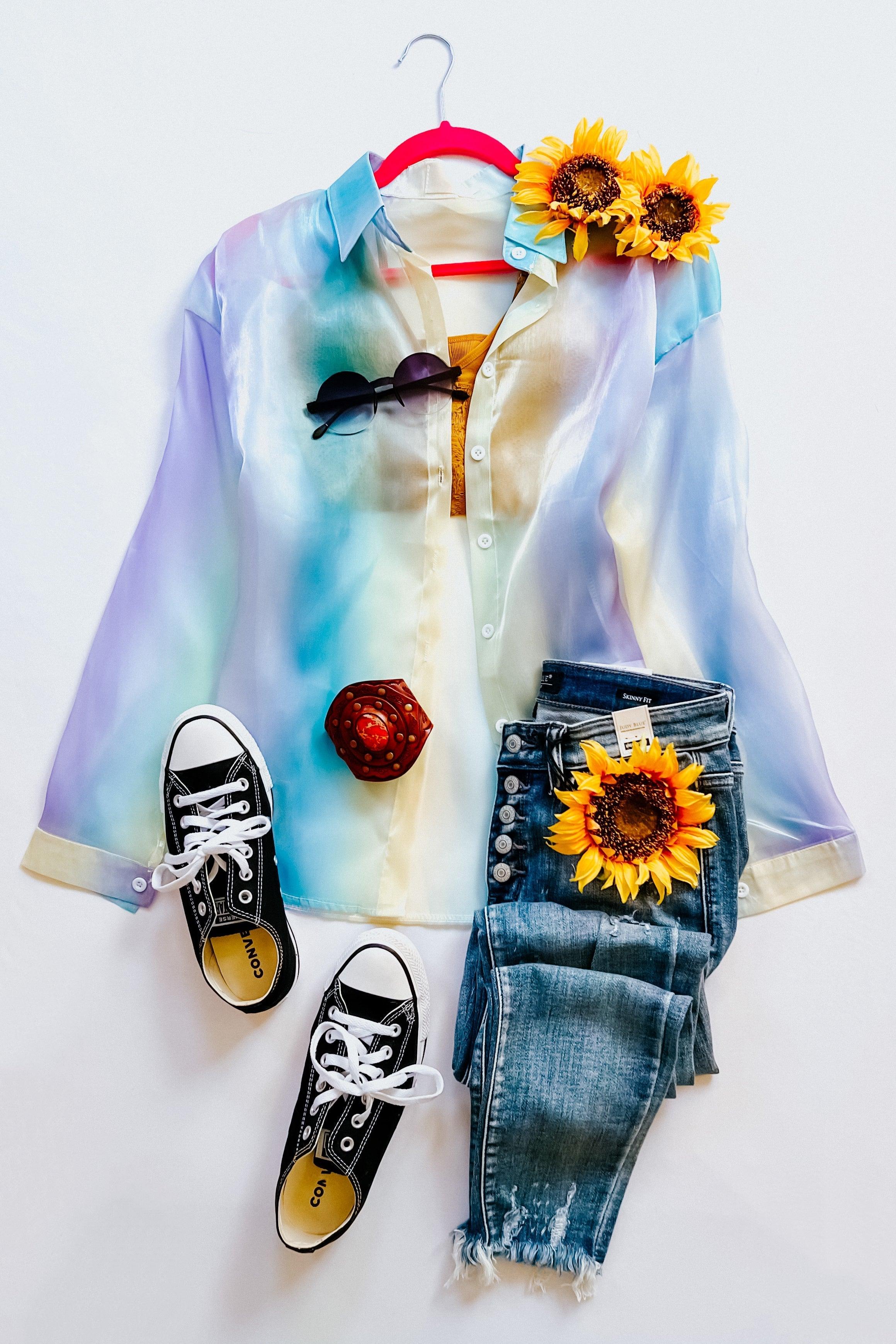 Light blue and pastel gradient sheer button-up top paired with distressed high-rise jeans, black canvas sneakers, sunglasses, and sunflowers on white background.