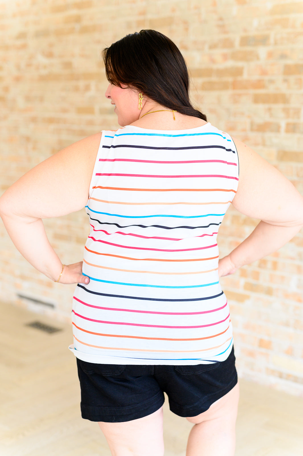 Plus size woman modeling ivory sleeveless tank with colorful horizontal stripes and black shorts against brick wall