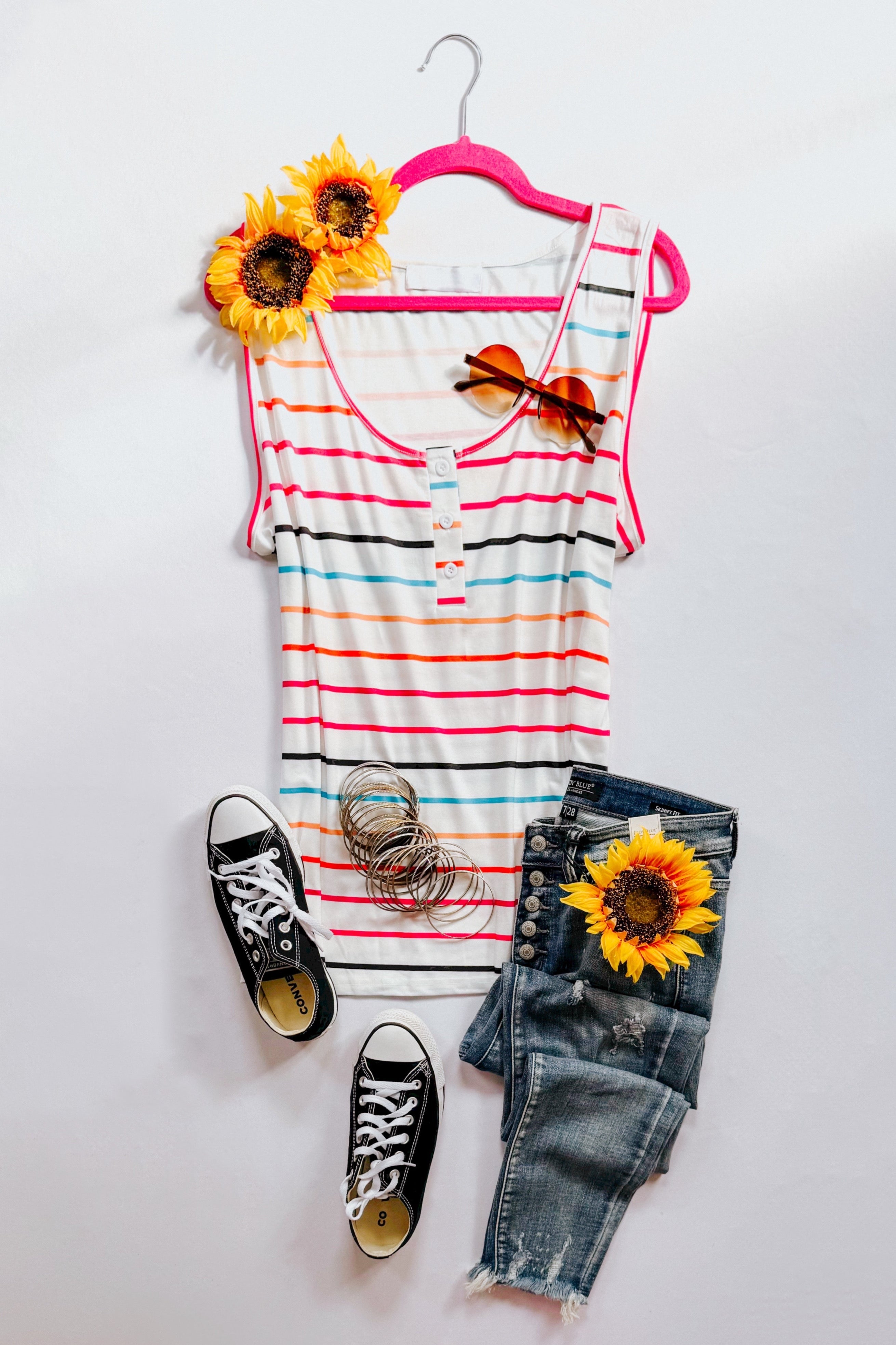 Ivory sleeveless colorful striped henley tank with denim shorts, sunglasses, black sneakers, and sunflowers flat lay