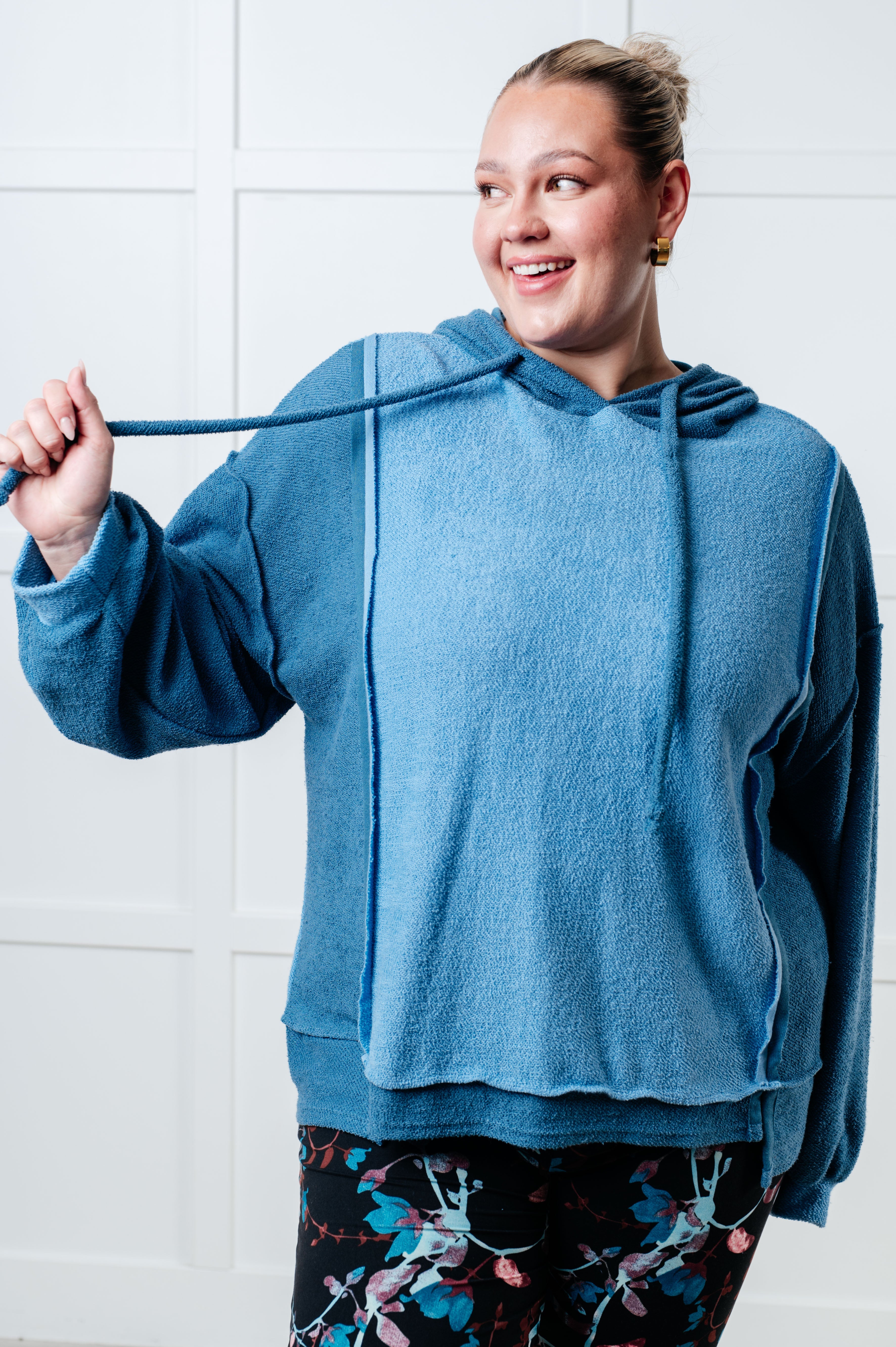 Smiling woman wearing a blue color block hoodie with a textured fabric and relaxed fit, paired with floral patterned leggings indoors.