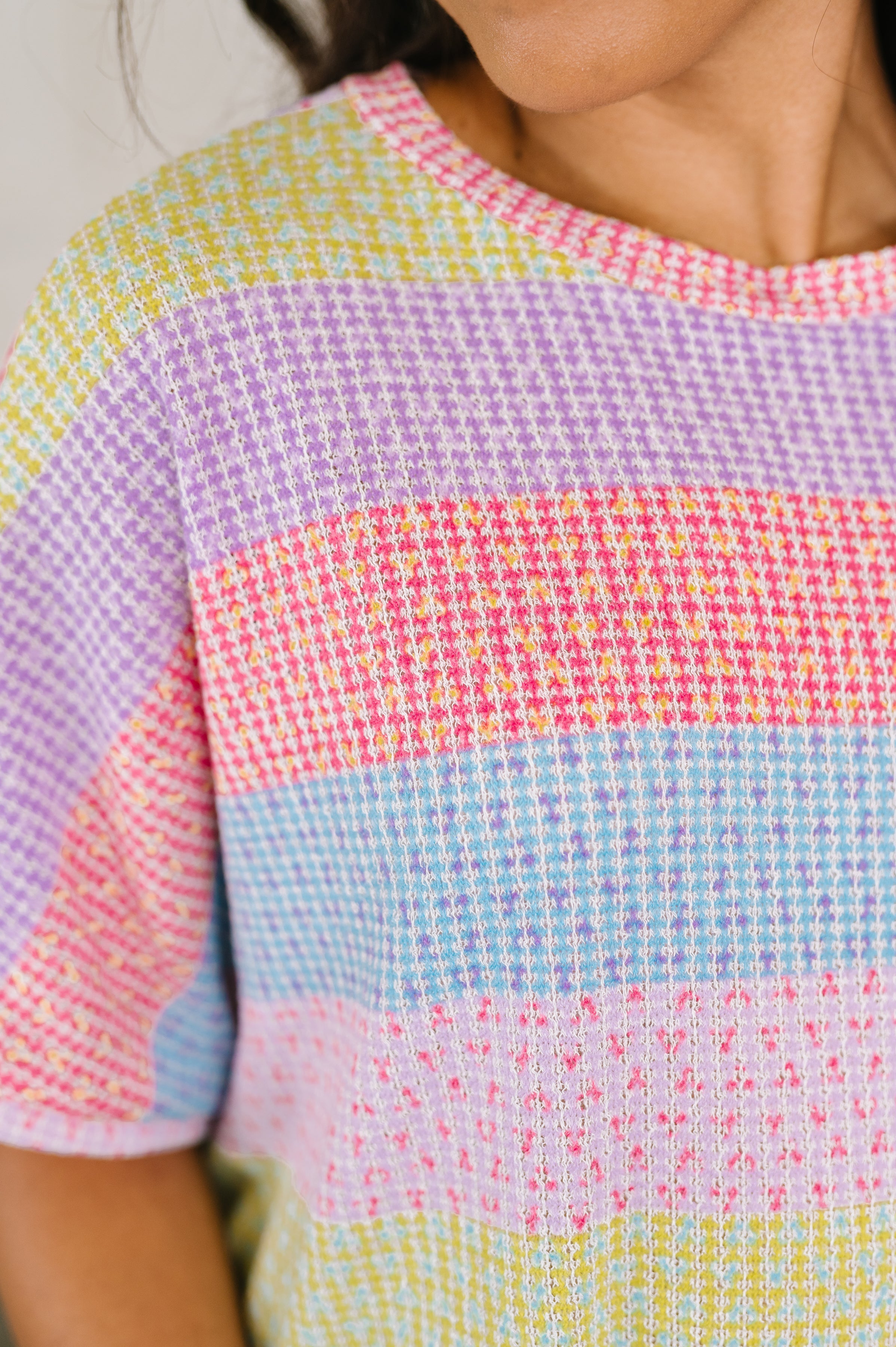 Close-up of colorful textured knit top with pastel stripes in pink, purple, blue, and yellow hues on model's upper torso
