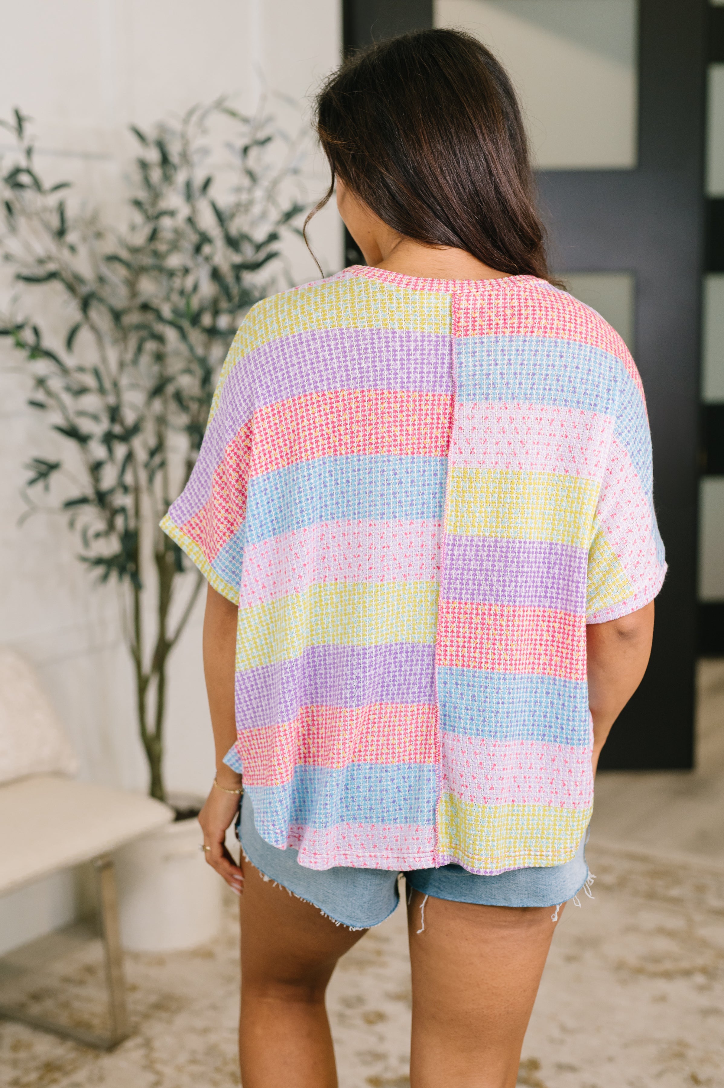 Back view of relaxed pastel striped textured top with short dolman sleeves worn with denim shorts indoors