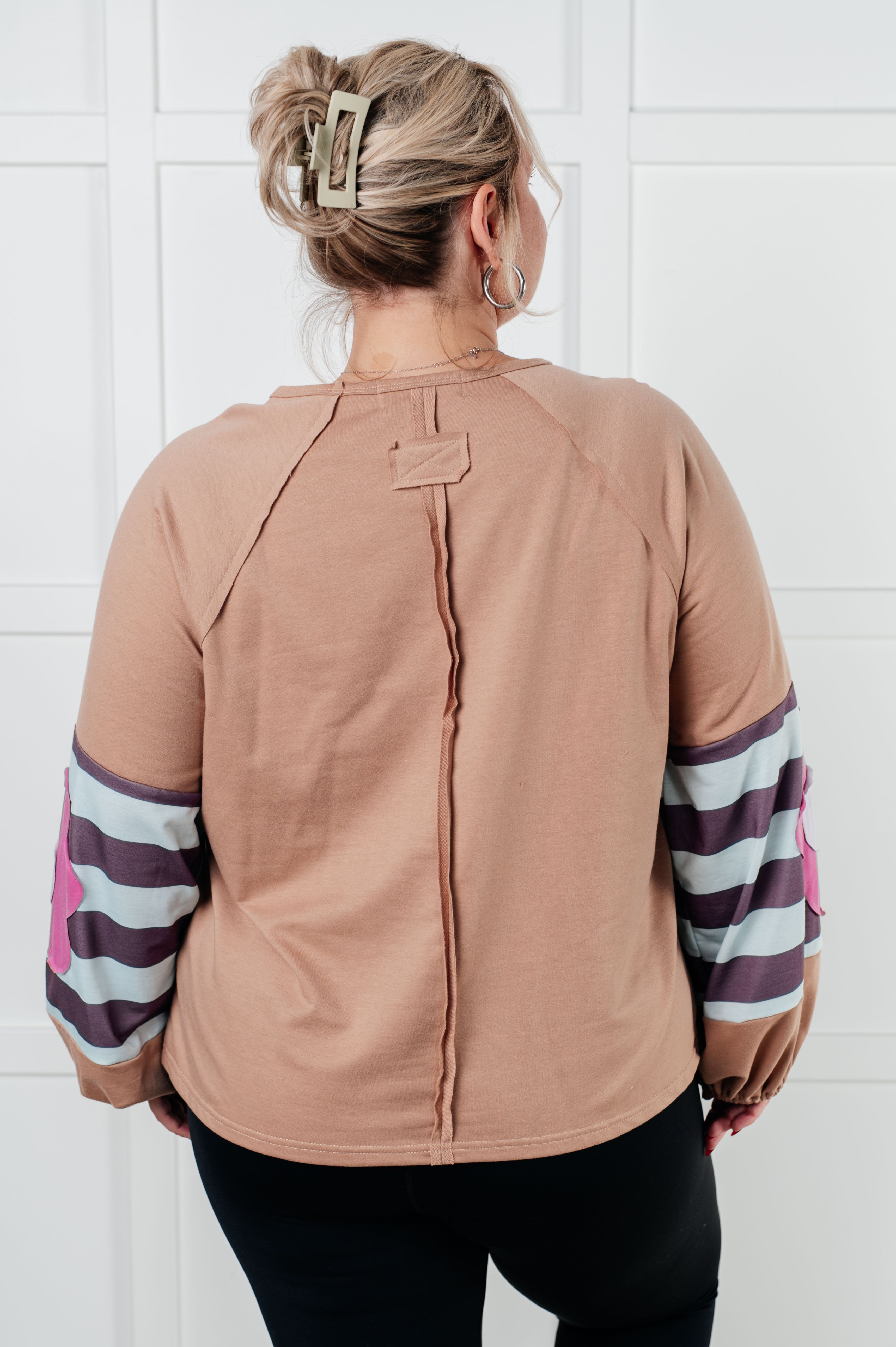 Back view of beige top with striped balloon sleeves featuring pink floral patch worn by woman indoors