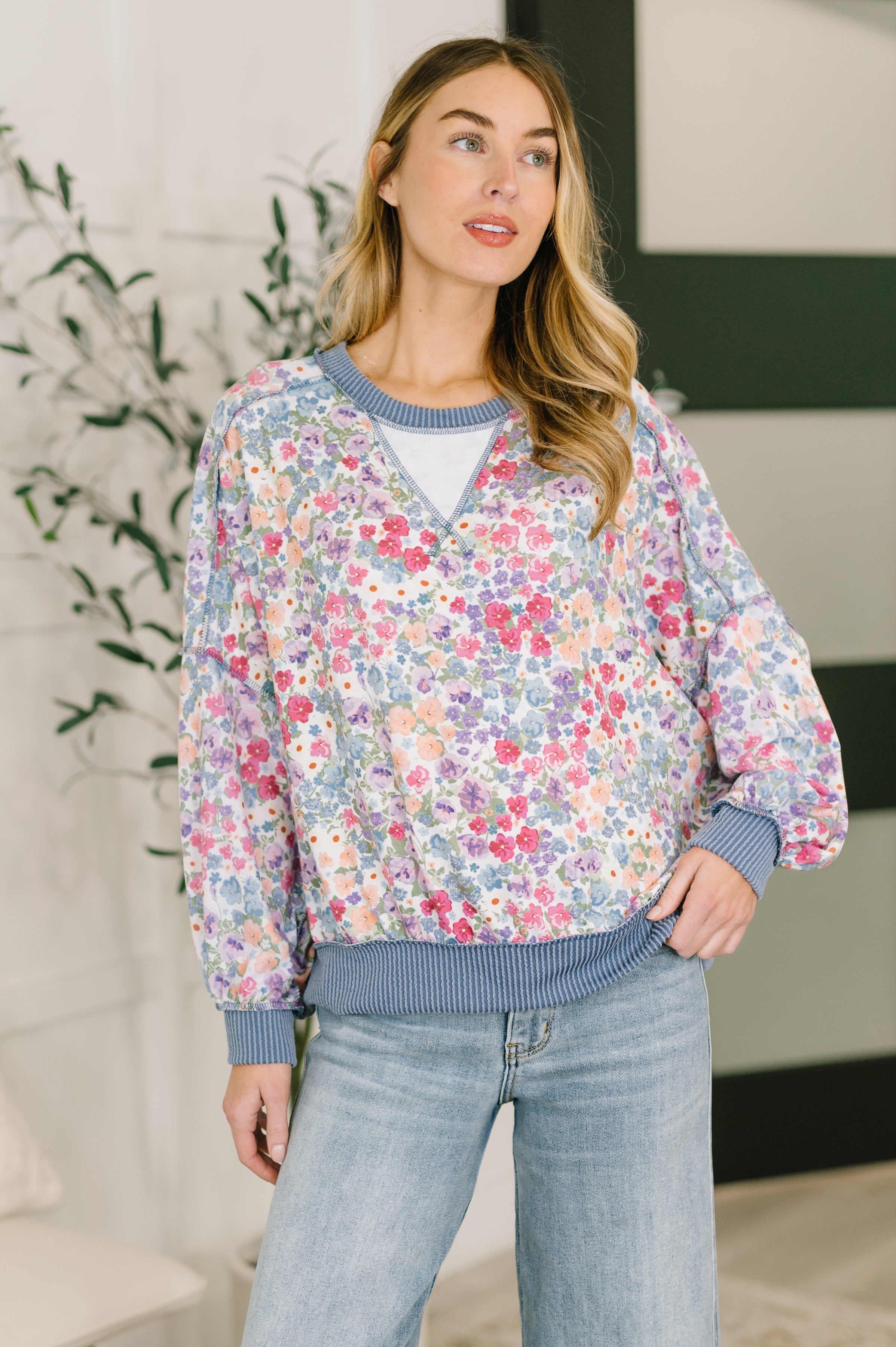 Woman wearing a blue floral pullover with ribbed trim and light wash jeans in a bright indoor setting