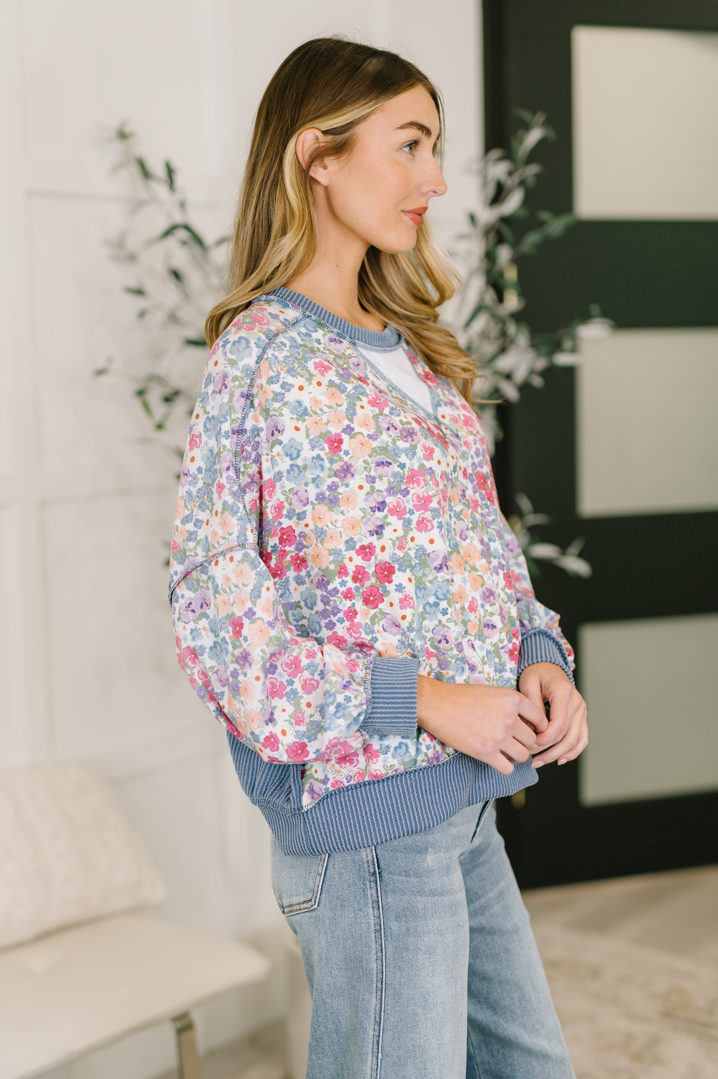Woman wearing a blue floral pullover with ribbed neckline, cuffs, and hem paired with light wash jeans indoors