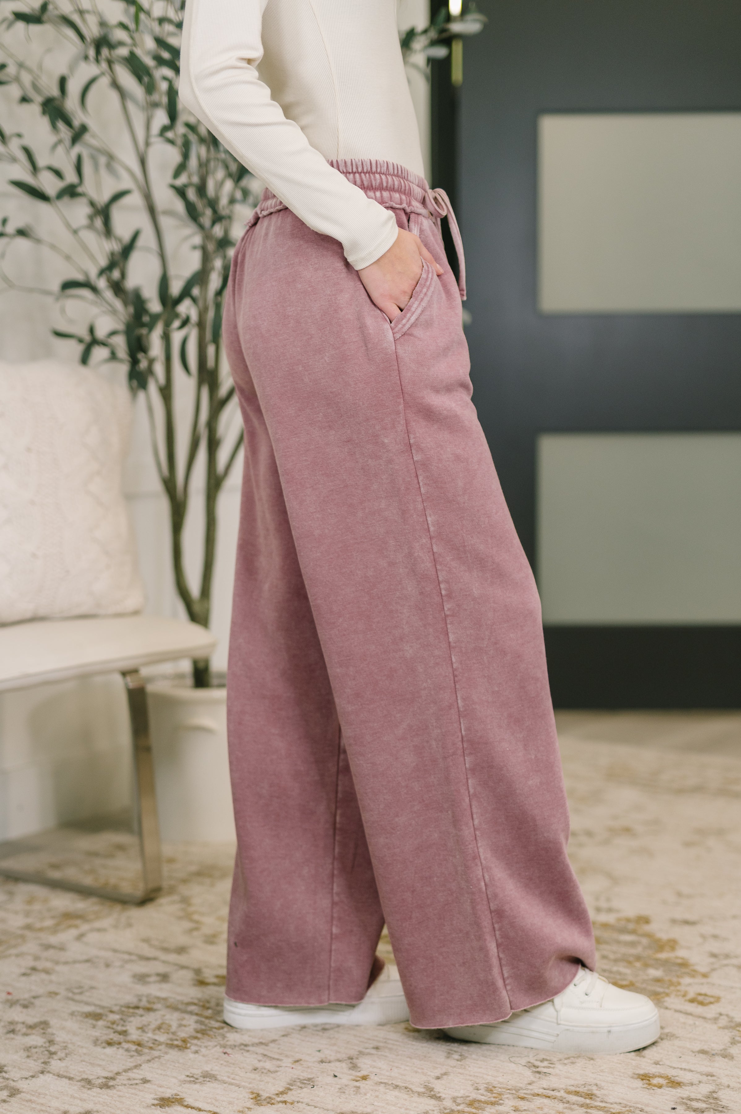 Side view of woman wearing light rose high waist wide-leg palazzo sweatpants with drawstring and pockets indoors