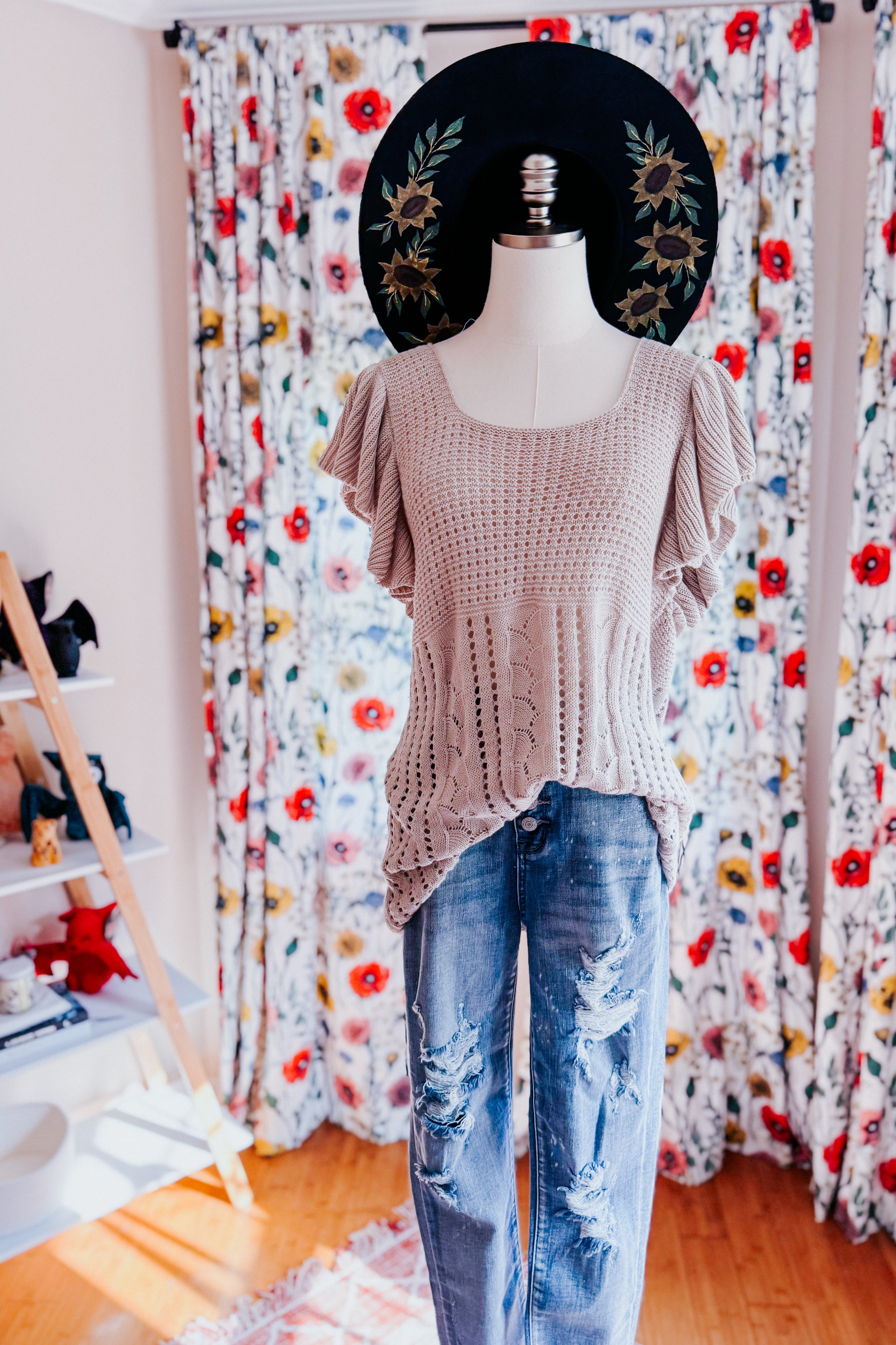 Grey pointelle knit top with flutter sleeves paired with distressed light blue jeans on a mannequin in a room with floral curtains and wooden floor.