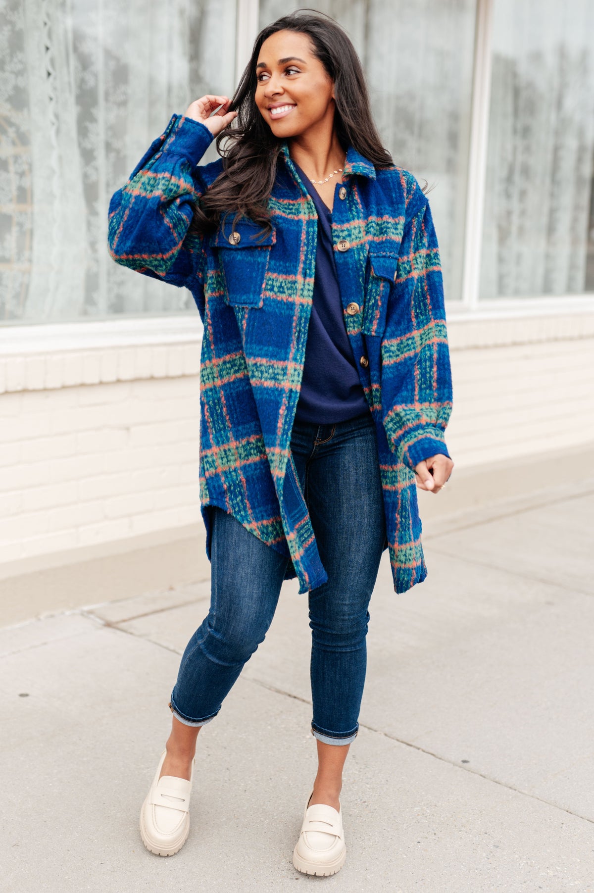 Woman modeling a blue plaid brushed flannel coat over a navy top and cuffed jeans with white loafers outdoors
