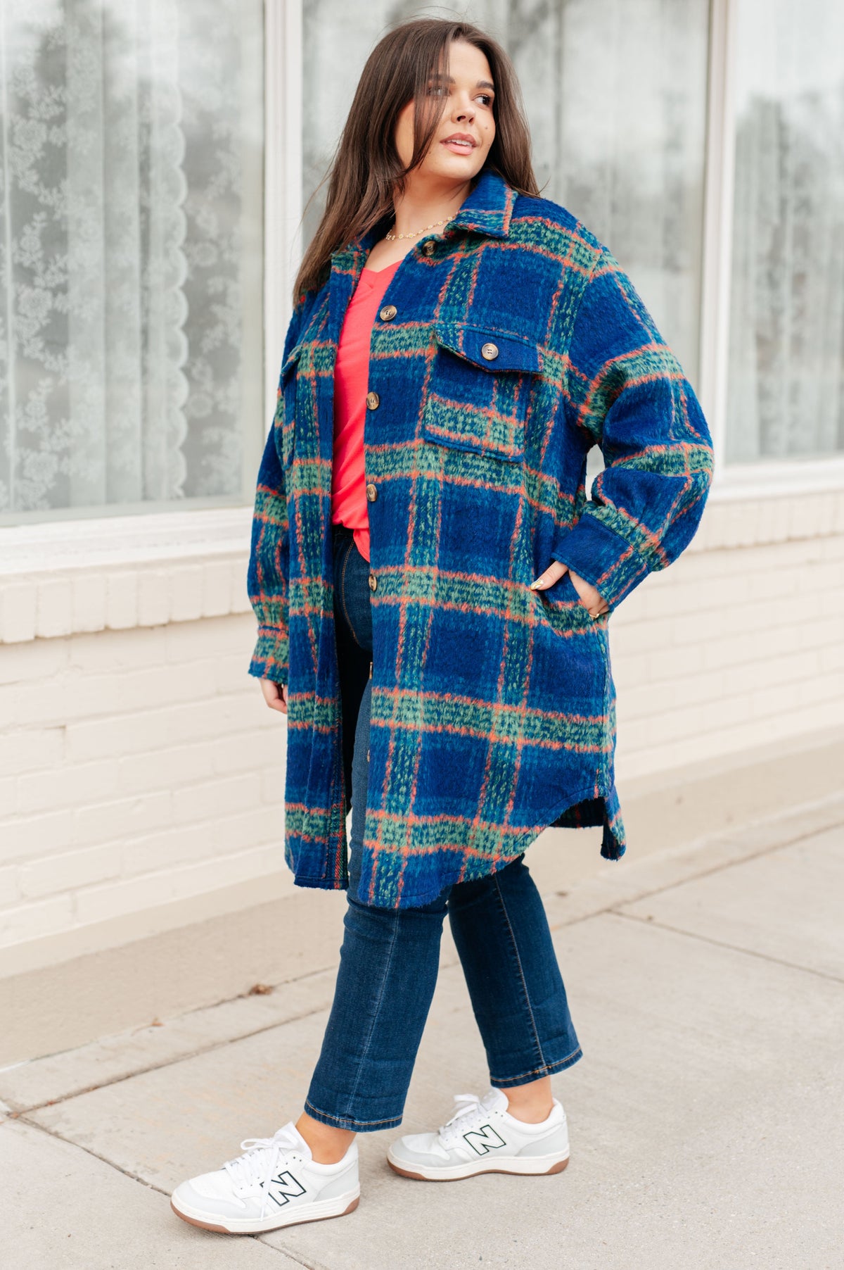 Woman wearing a blue plaid brushed flannel coat over a red top with cropped jeans and white sneakers outside a windowed building
