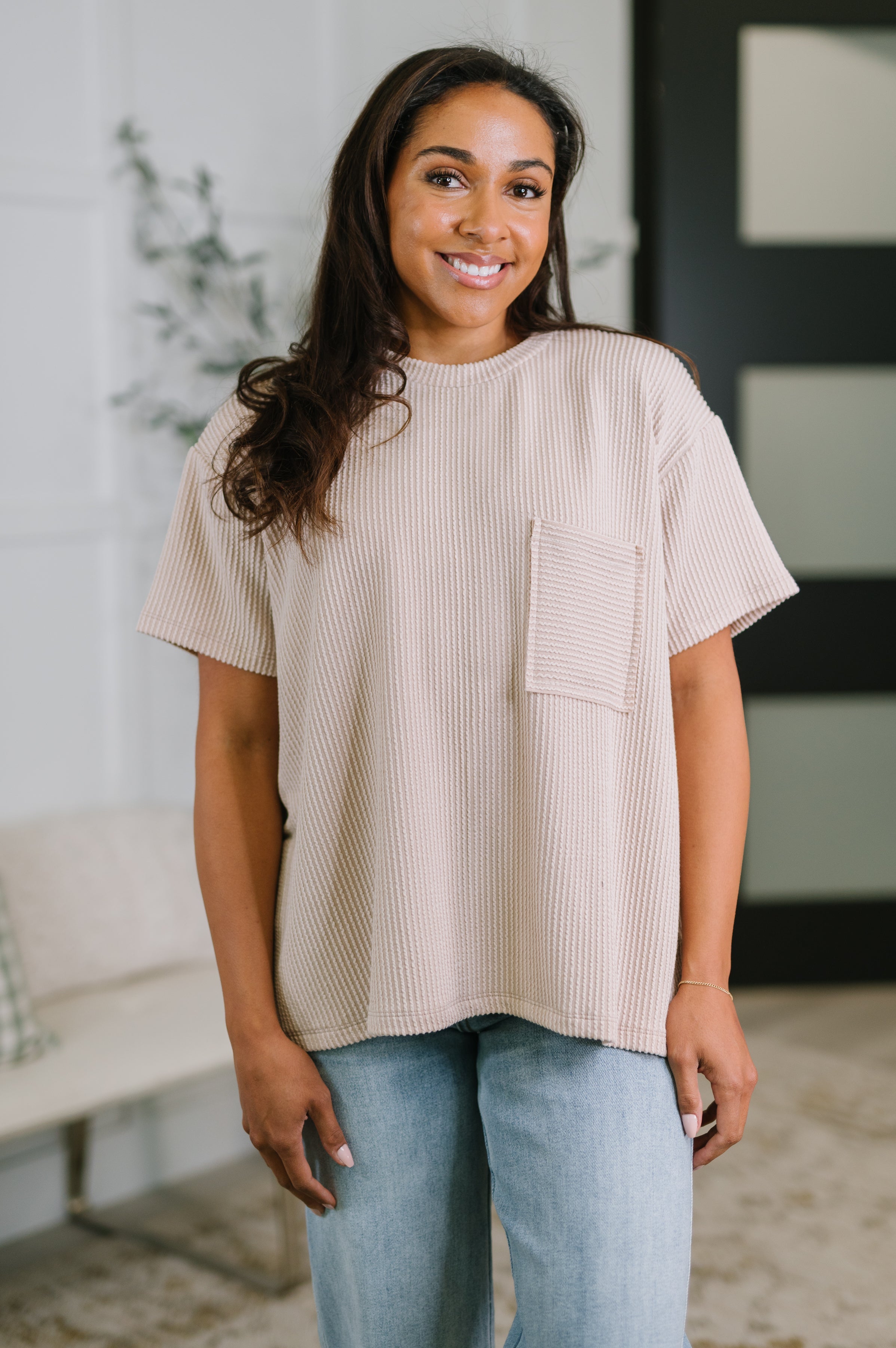 Smiling woman wearing ash mocha textured boxy tee with front pocket paired with light wash jeans in bright indoor setting