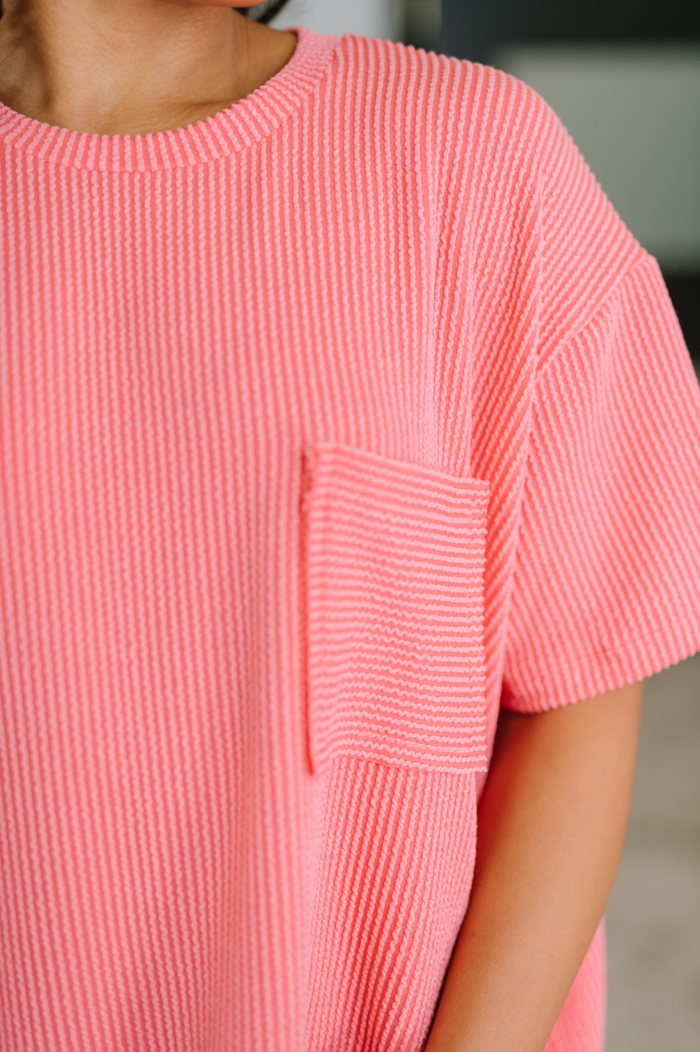 Close-up of salmon textured boxy tee with chest pocket worn by person with arm relaxed at side indoors