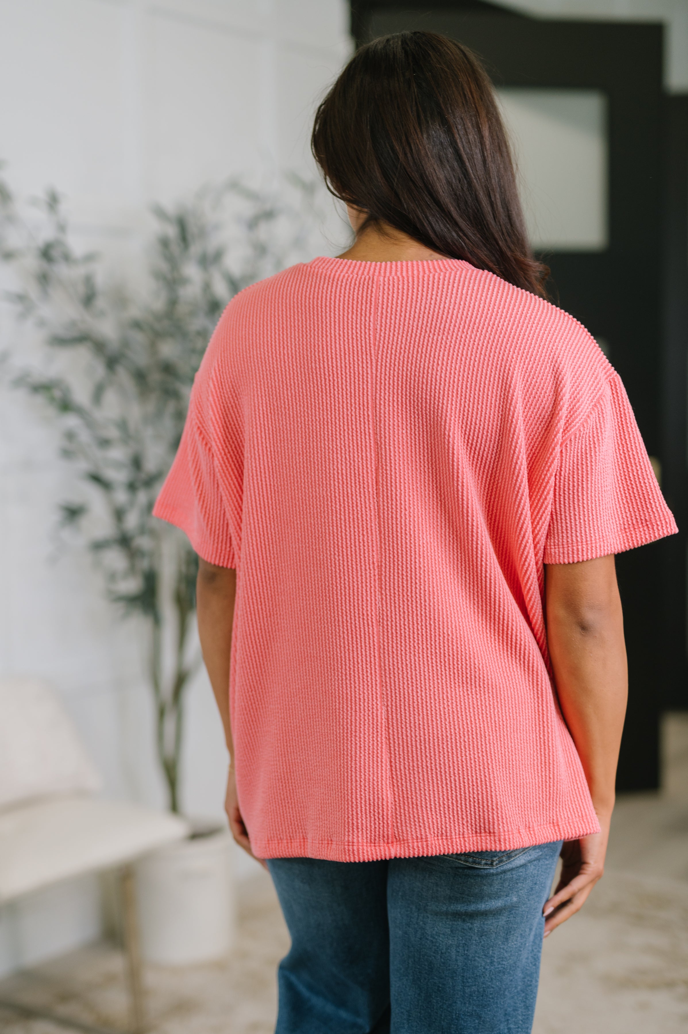 Back view of person wearing salmon textured boxy tee with short sleeves paired with blue jeans indoors