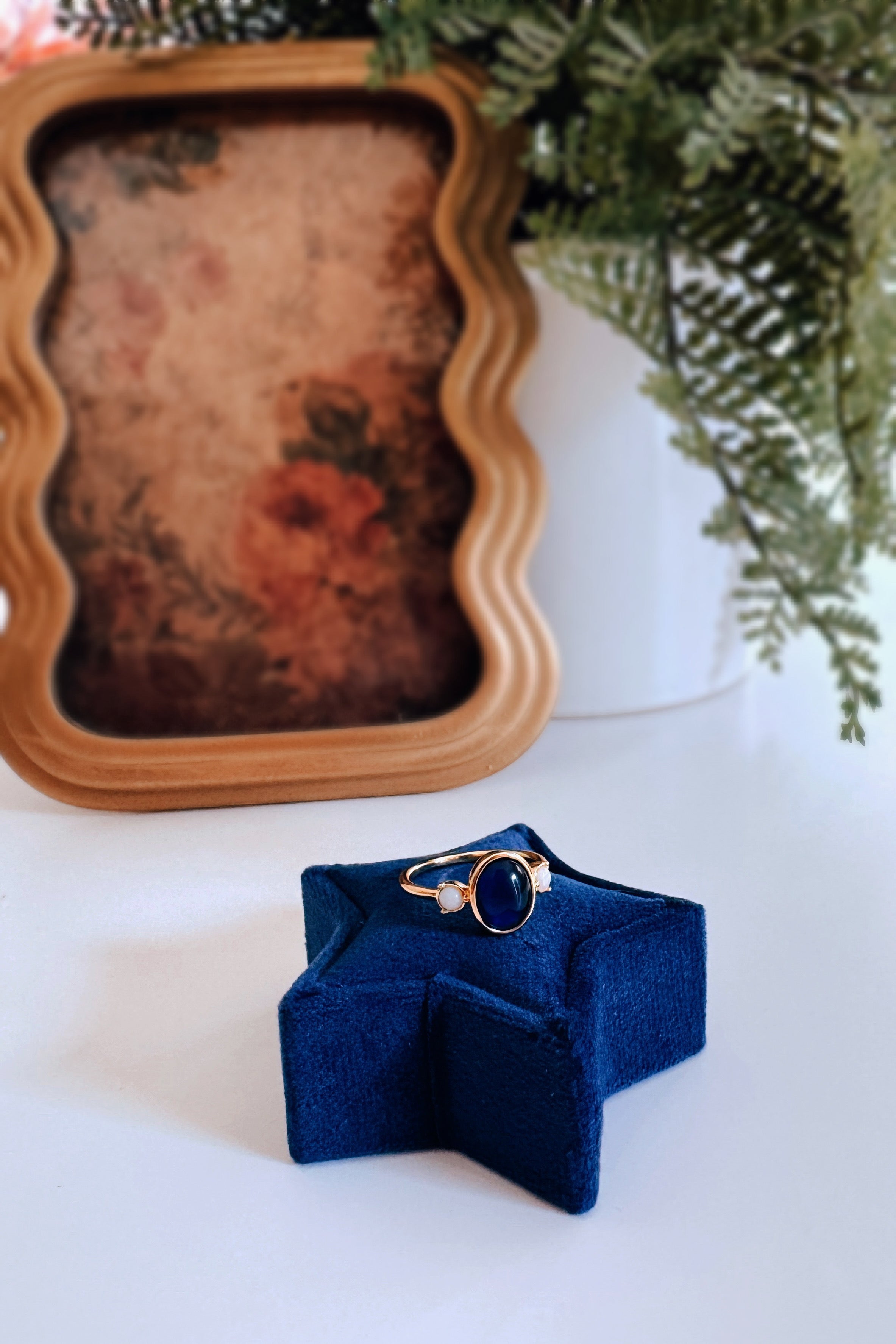 Gold ring with dark oval stone and two small pale round stones resting on blue star-shaped velvet stand