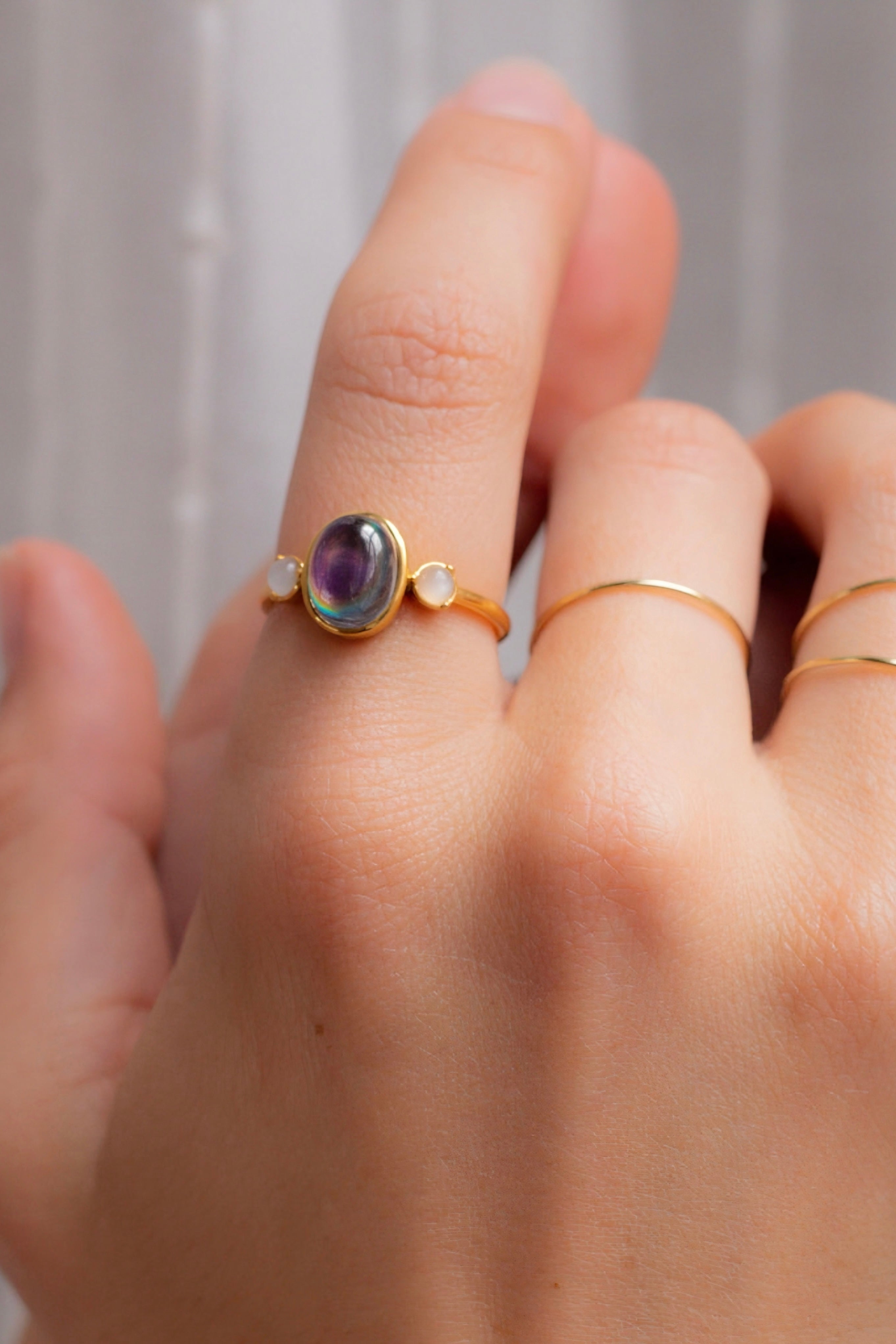 Gold ring with an iridescent oval stone and two small round stones worn alongside slim gold bands on finger