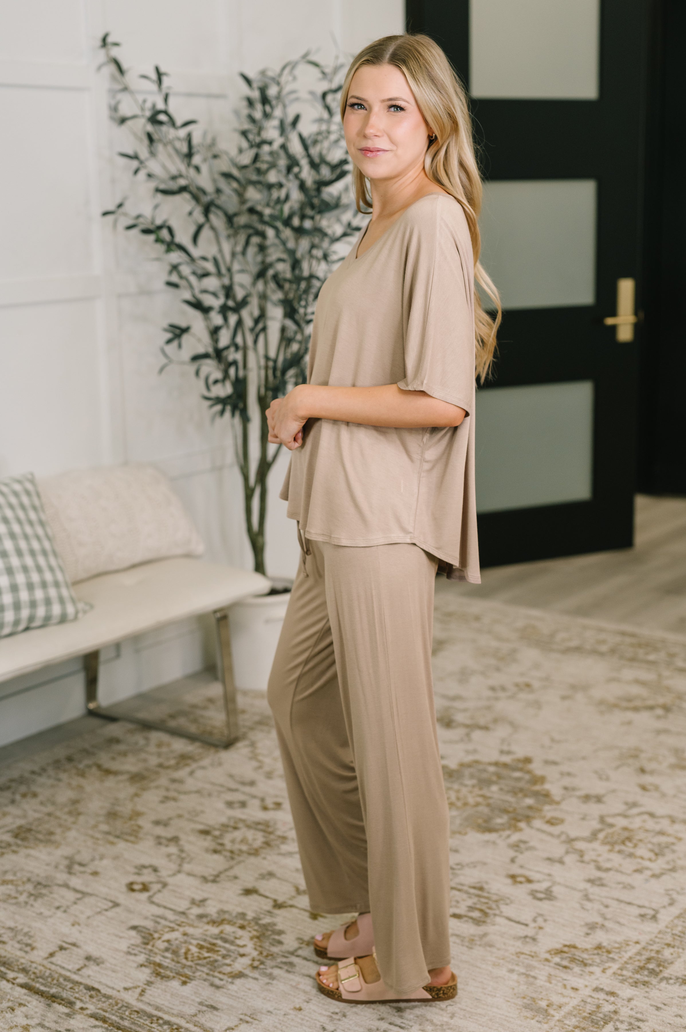 Woman in relaxed beige lounge set with loose top and wide-leg pants standing indoors on patterned rug