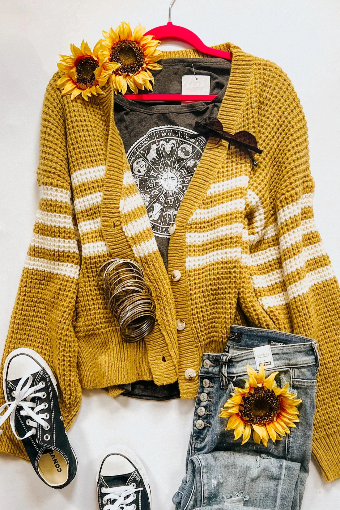 Mustard knit cardigan with white stripes paired with graphic tee, distressed jeans, black sneakers, bracelets, and sunflower accents