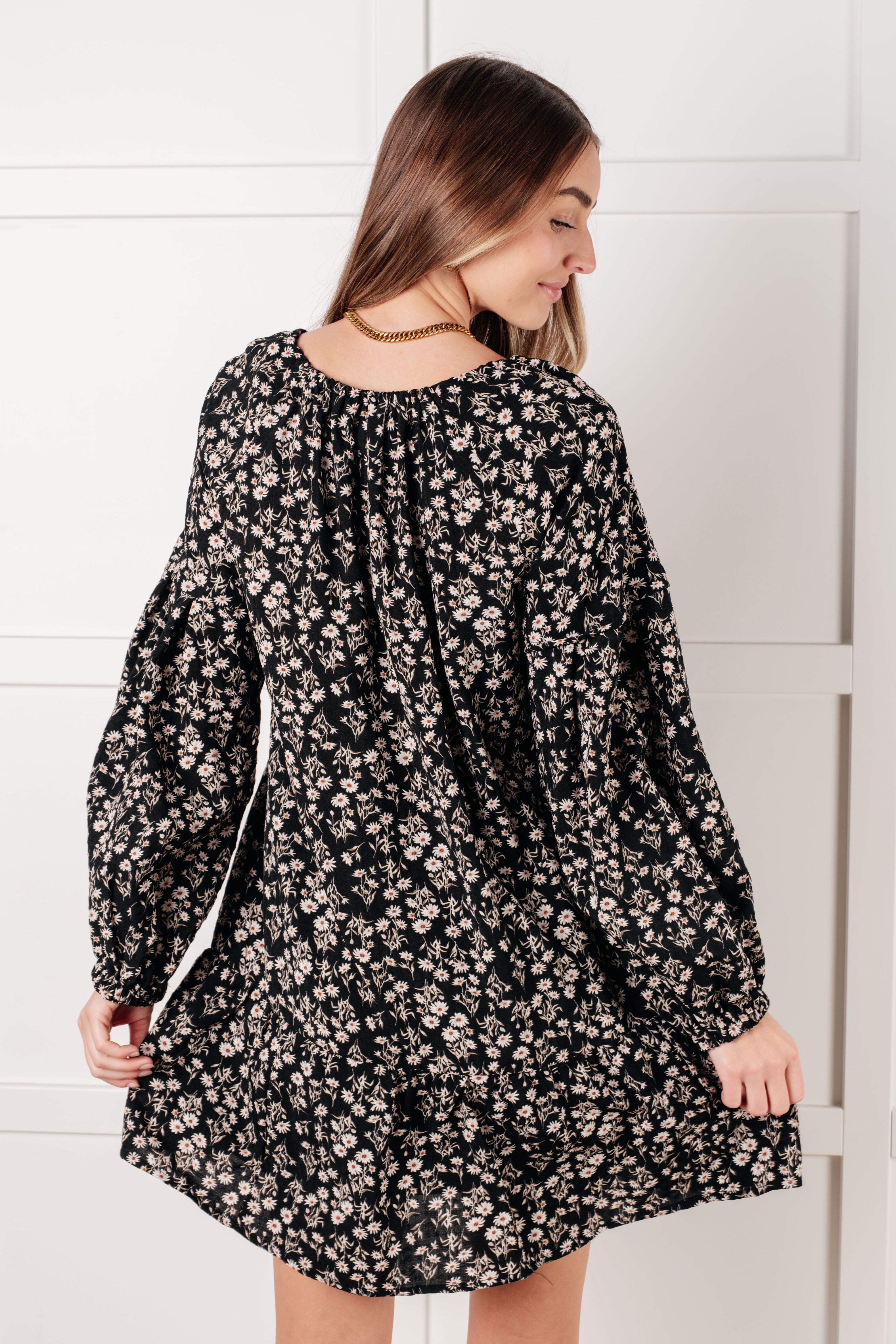 Woman wearing black floral dress with long puff sleeves shown from the back in a bright indoor setting