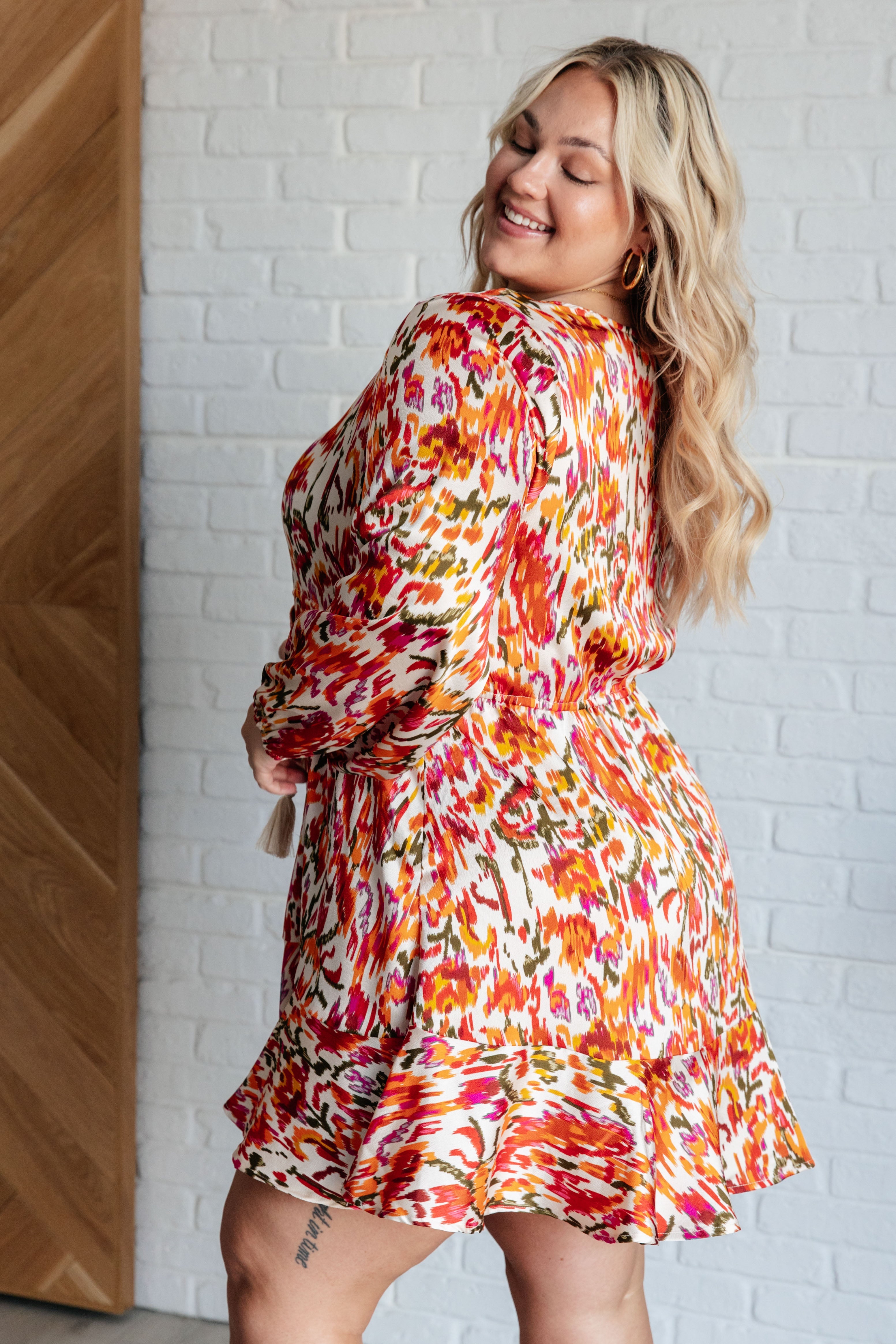 Plus size woman smiling wearing colorful orange patterned dress with balloon sleeves and ruffle hem indoors