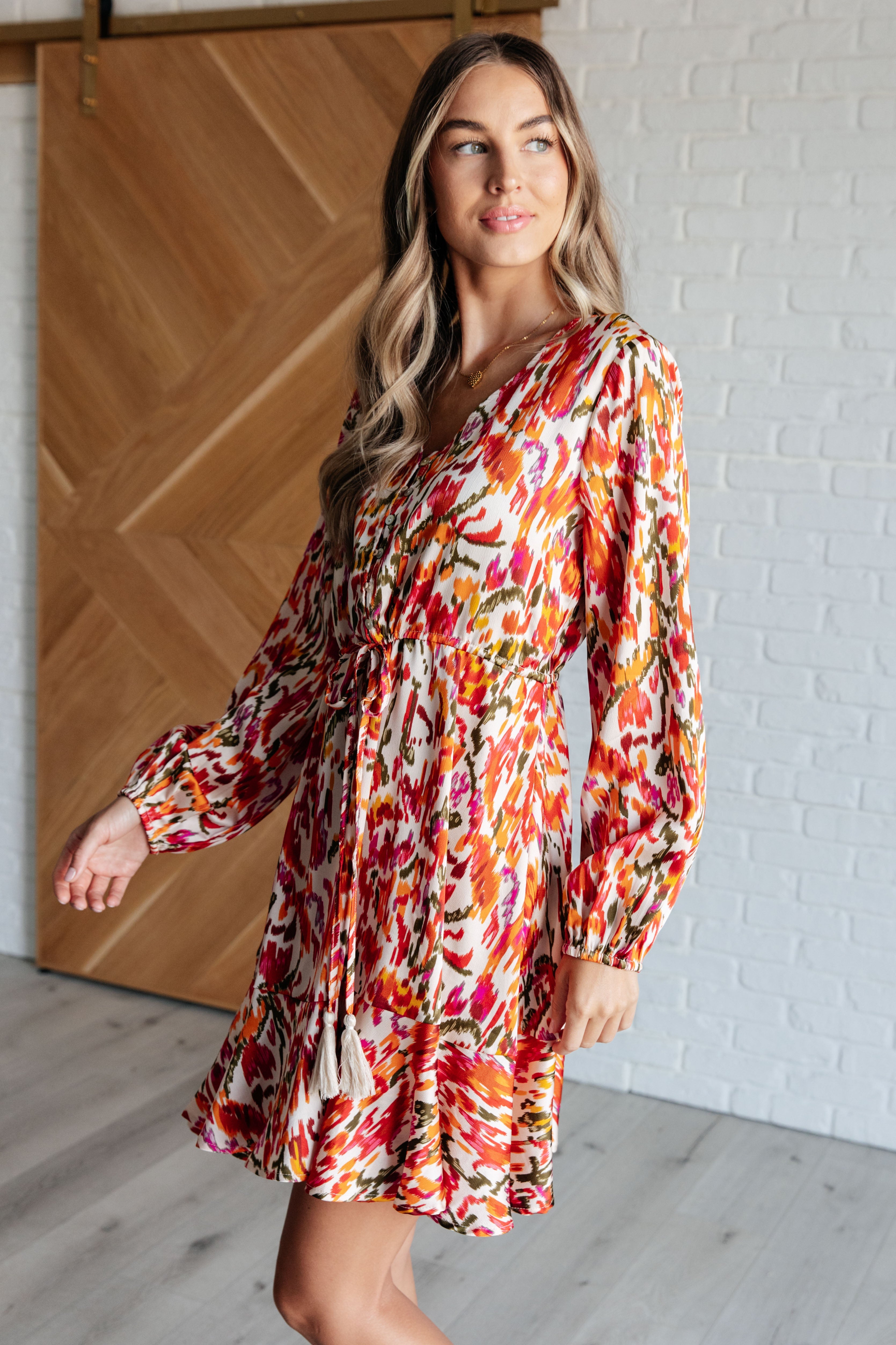 Woman wearing vibrant orange patterned dress with balloon sleeves and ruffled hem standing indoors