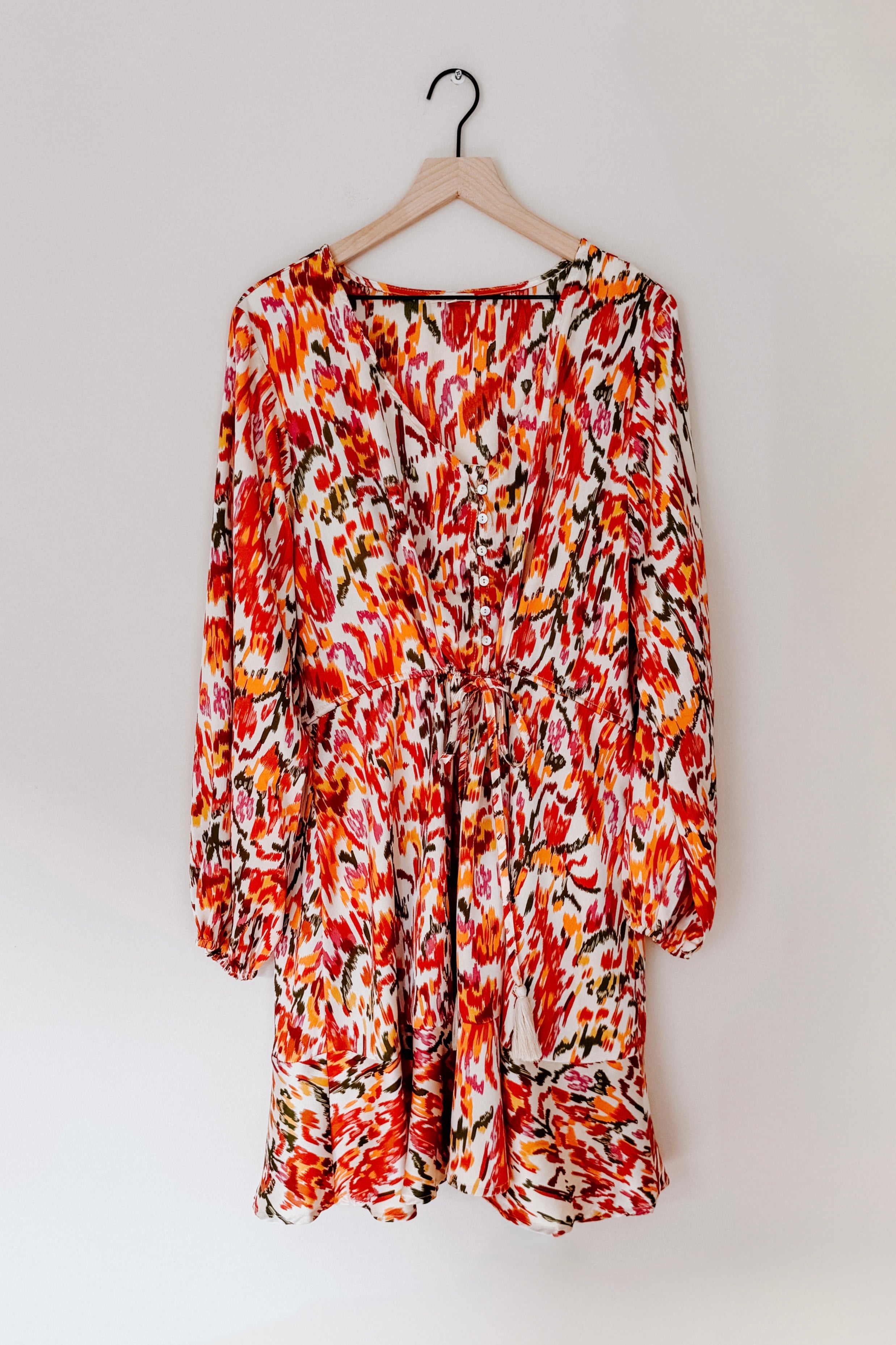 Orange patterned V-neck dress with balloon sleeves and gathered waist hanging on wooden hanger against white wall