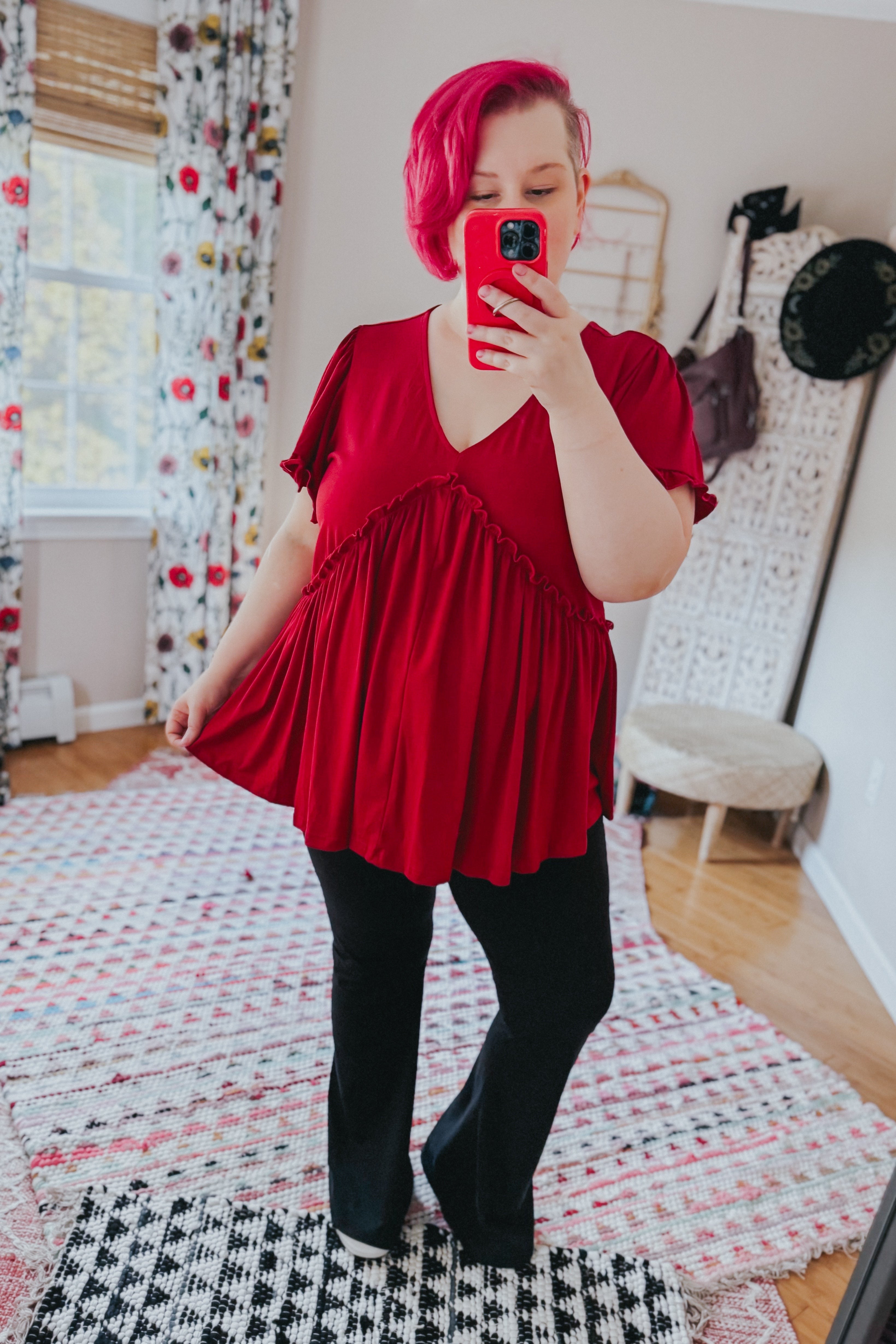 Woman with pink hair in free-spirited red V-neck top with ruffle detail paired with black pants in cozy room setting