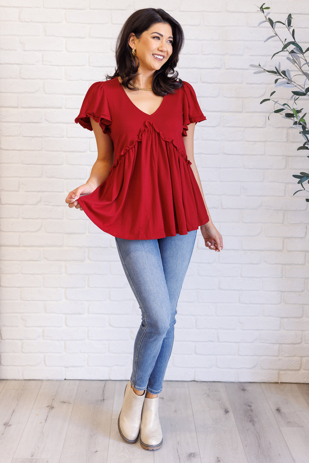 Woman wearing a size-inclusive red V-neck top with ruffle details and flutter sleeves, paired with light jeans and boots