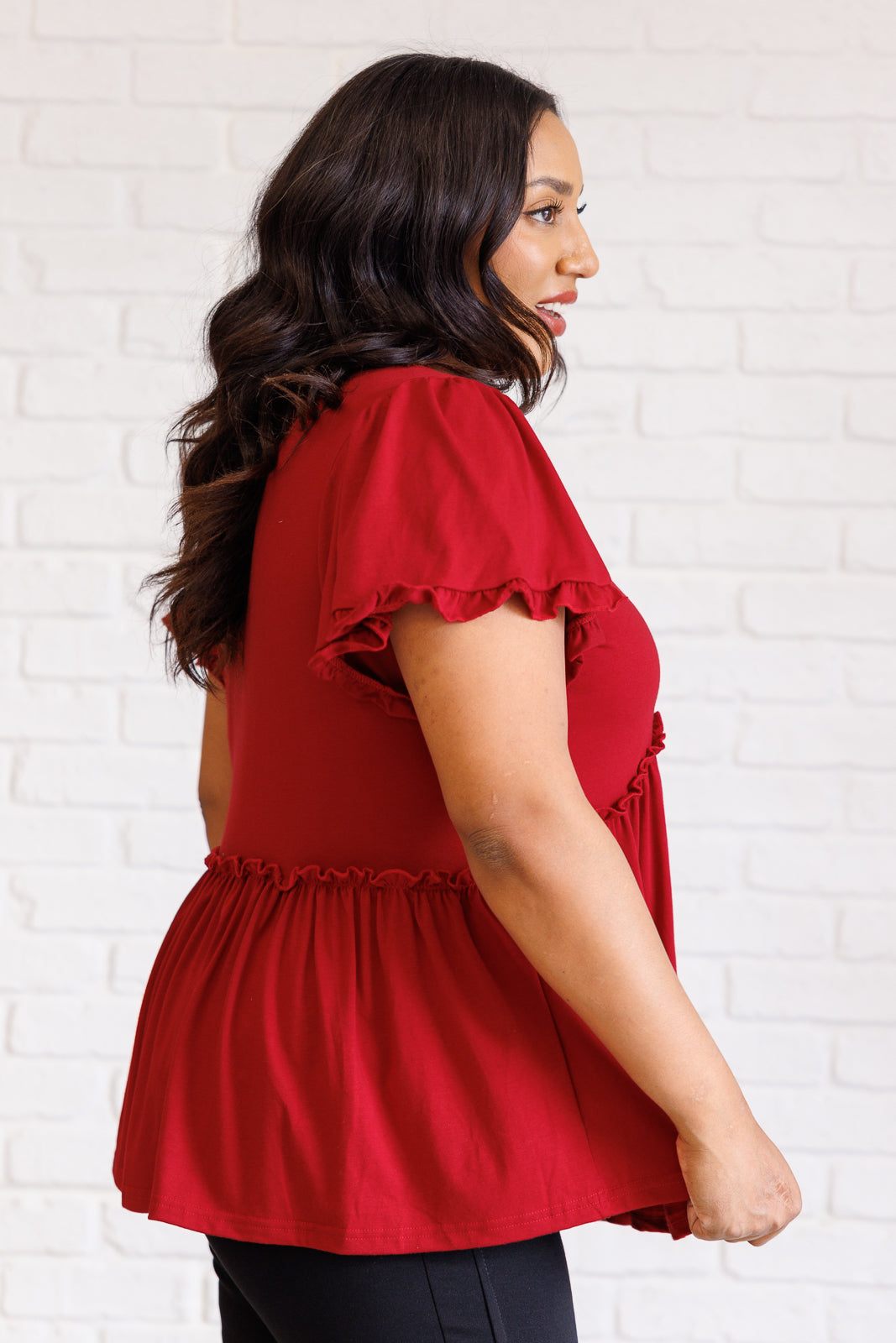 Curvy woman wearing size-inclusive red V-neck top with delicate ruffle details and flutter sleeves in bright studio setting