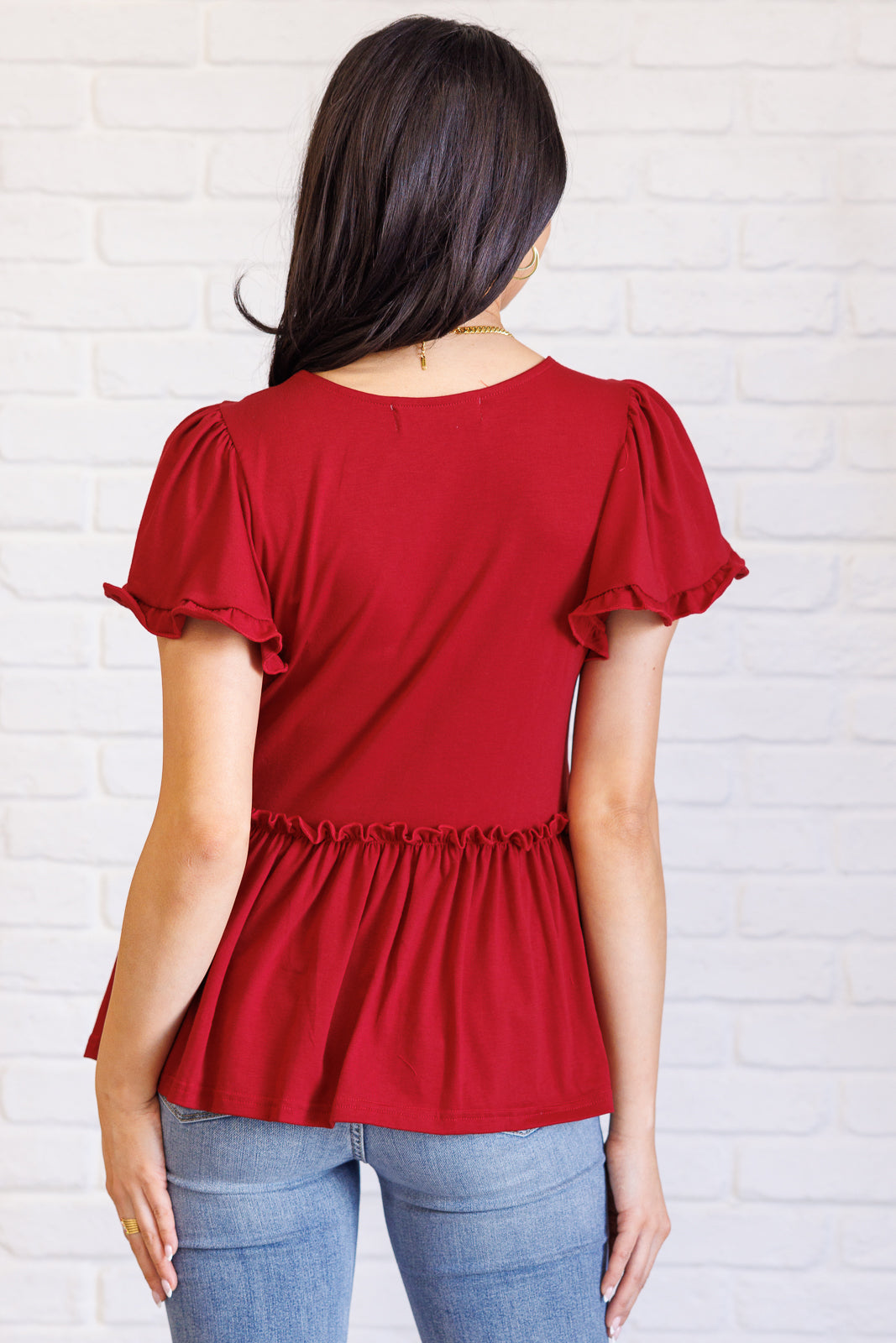 Woman seen from back wearing red top with ruffle sleeves and gathered waist paired with light blue jeans
