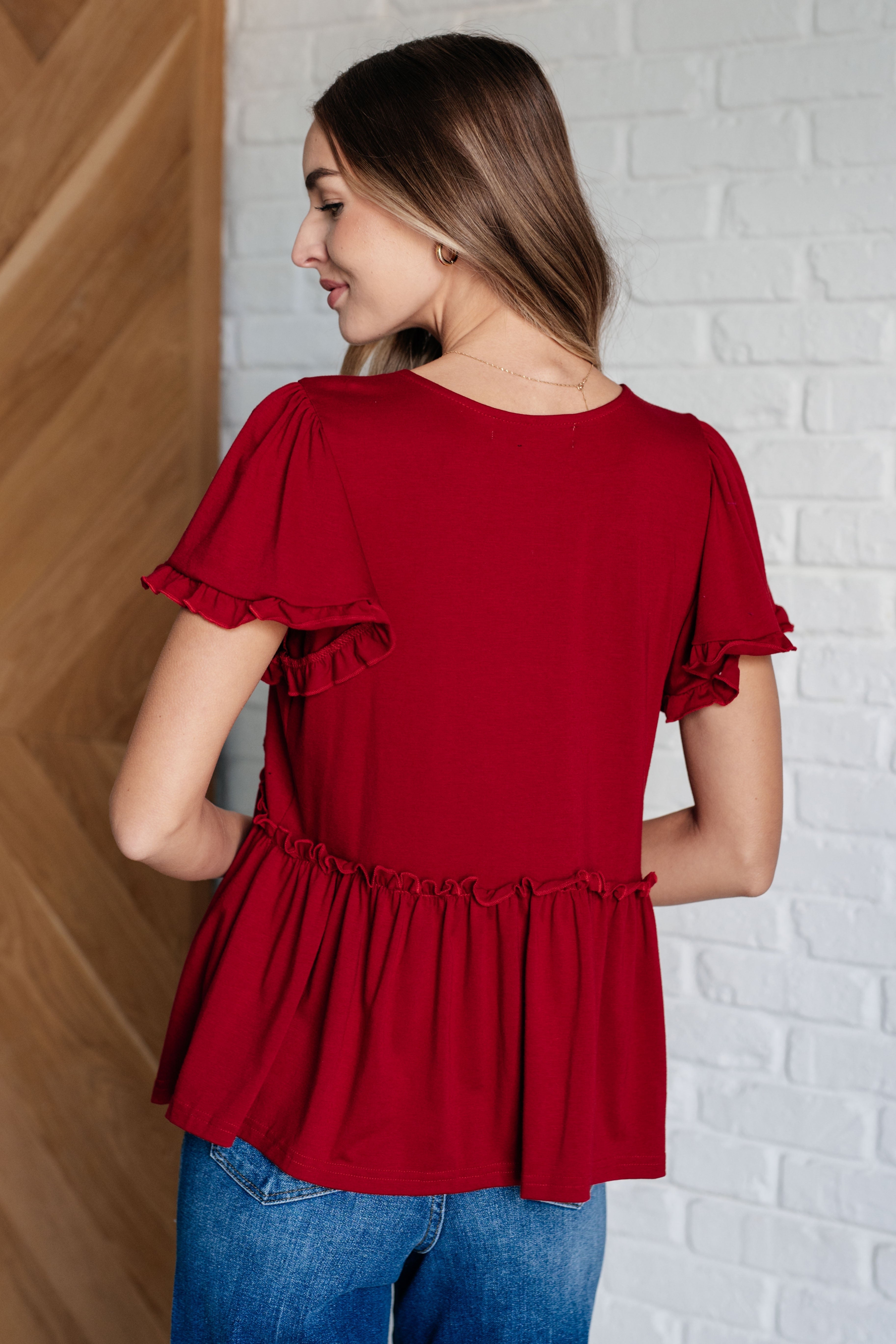 Woman wearing a bold red top with flutter sleeves and gathered waist paired with casual blue jeans in relaxed setting