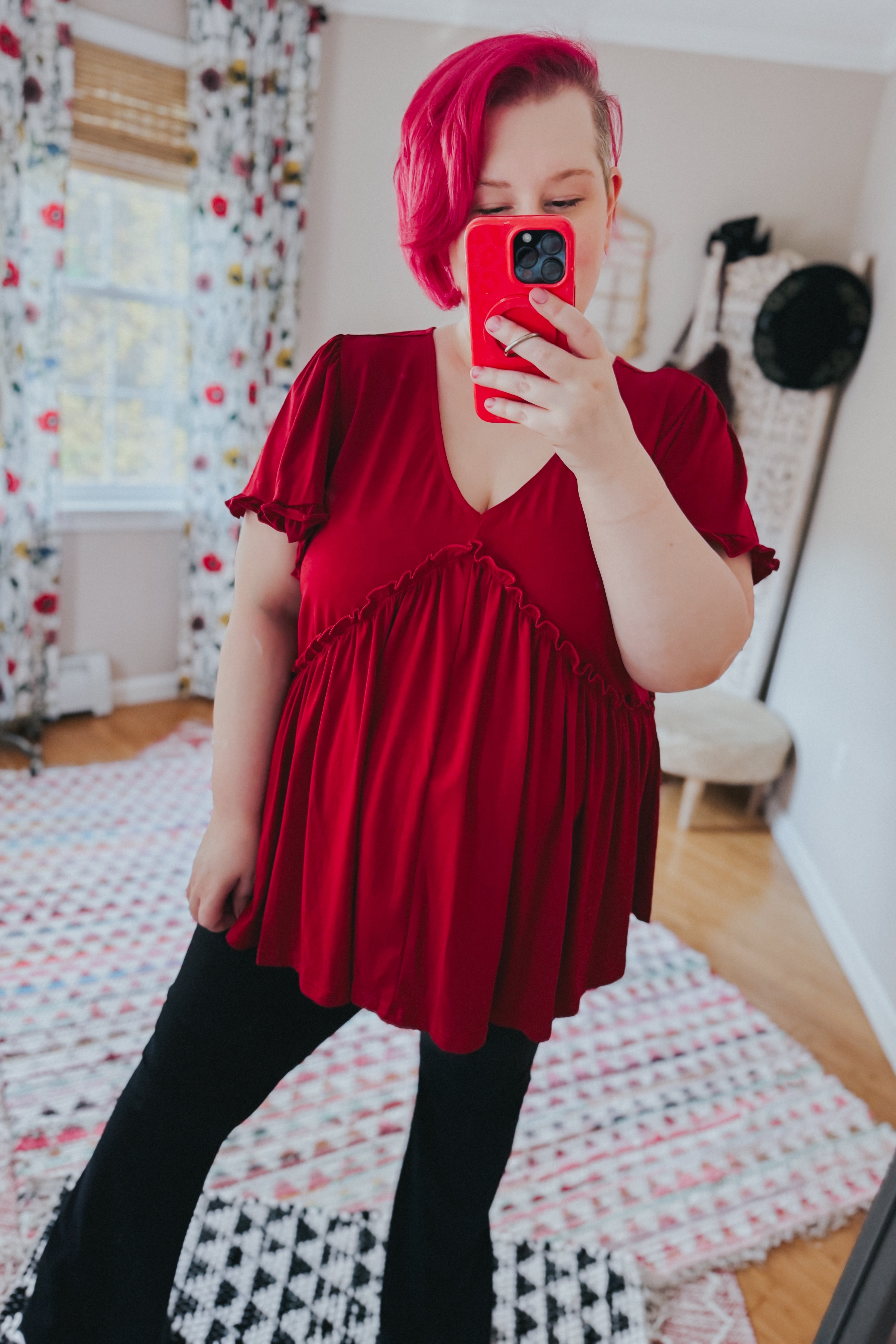 Woman wearing red V-neck top with ruffle detail and flutter sleeves paired with black pants in cozy room setting