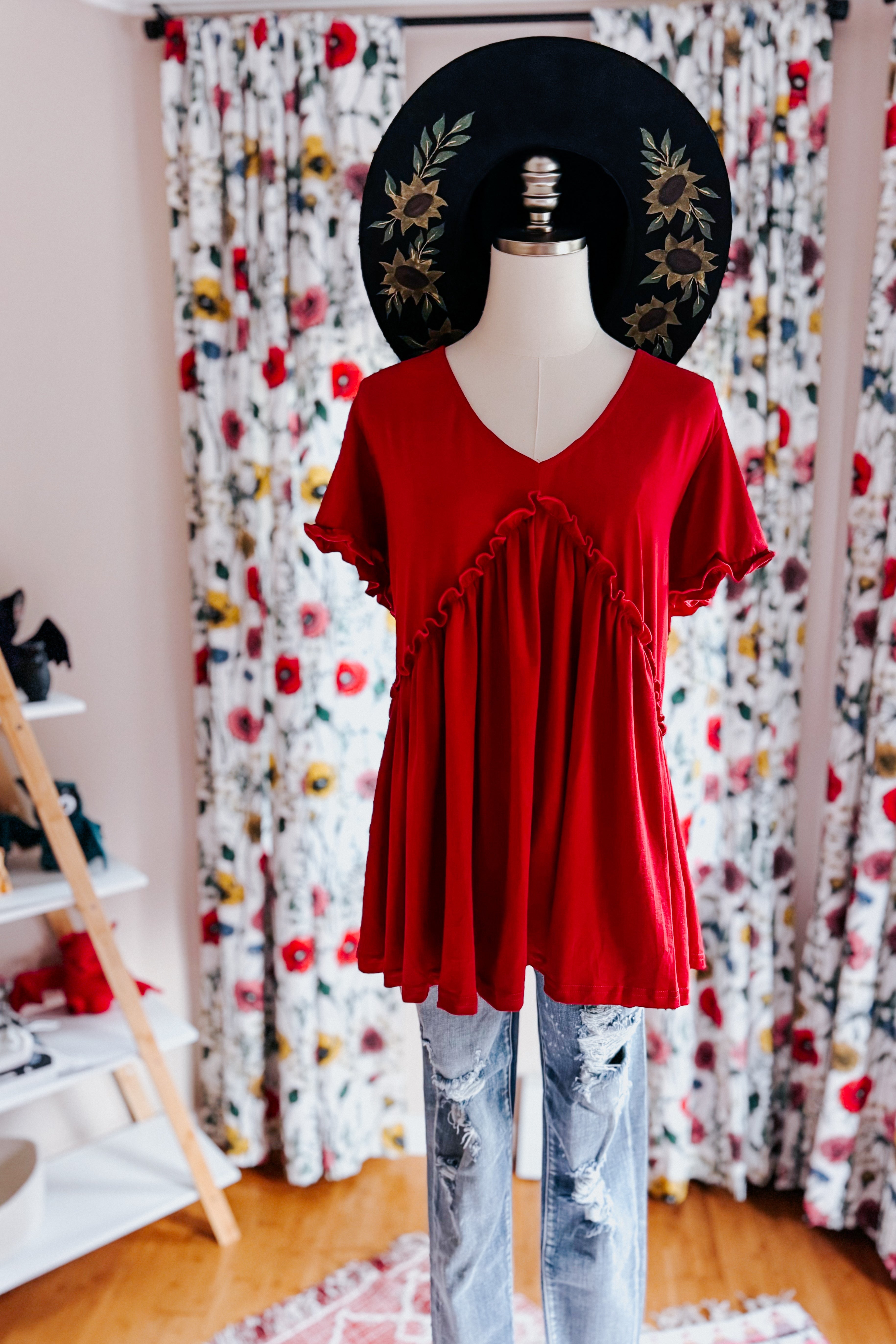 Red V-neck top with ruffle detail and flutter sleeves styled with distressed blue jeans on mannequin