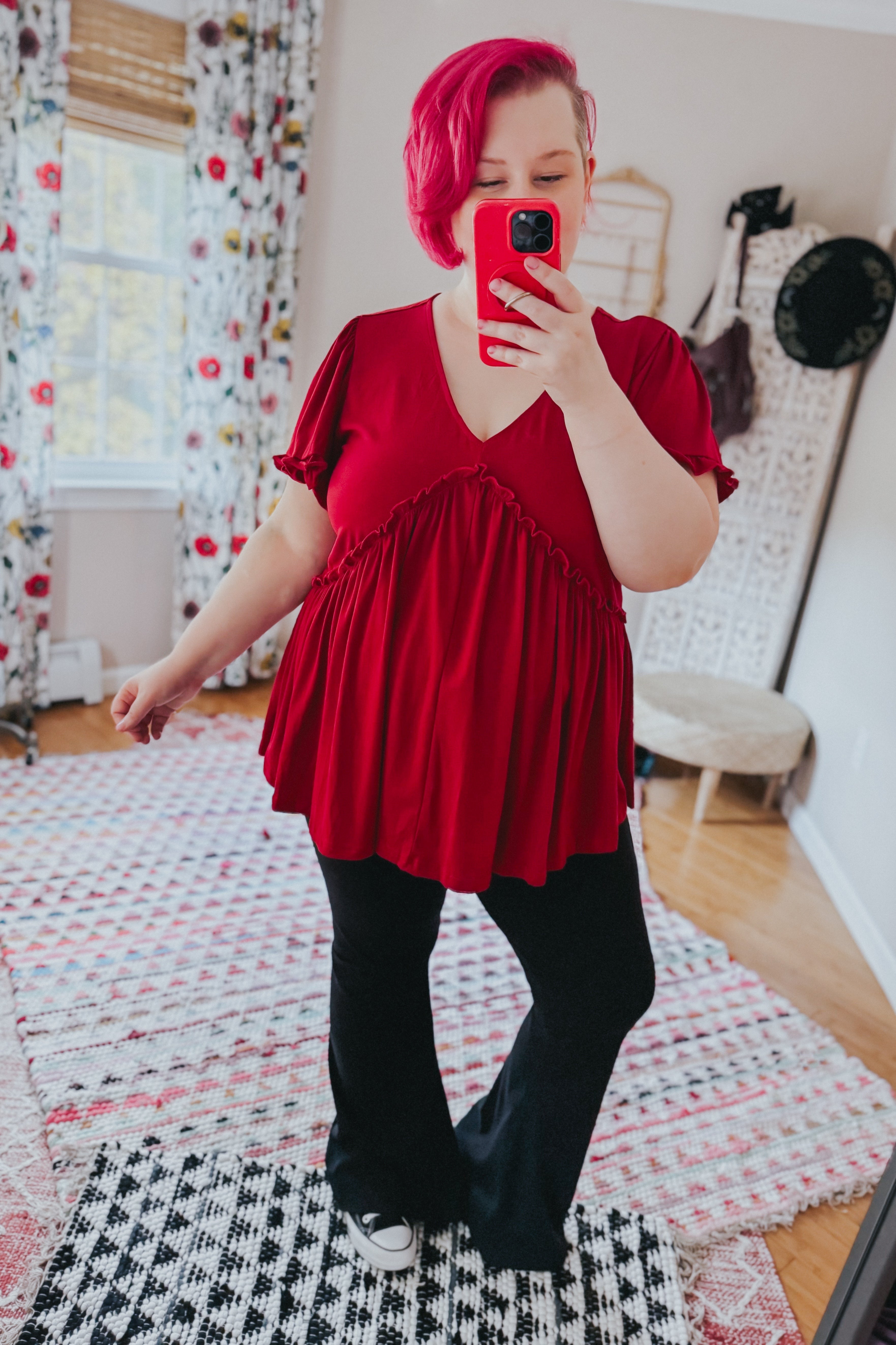 Woman wearing a free-spirited red V-neck top with ruffle details and flutter sleeves paired with black pants indoors