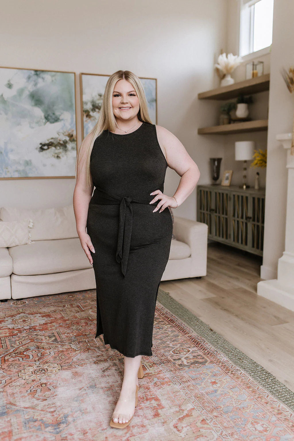 Curvy woman wearing a charcoal tie-waist midi dress standing confidently on a patterned rug in a modern living room