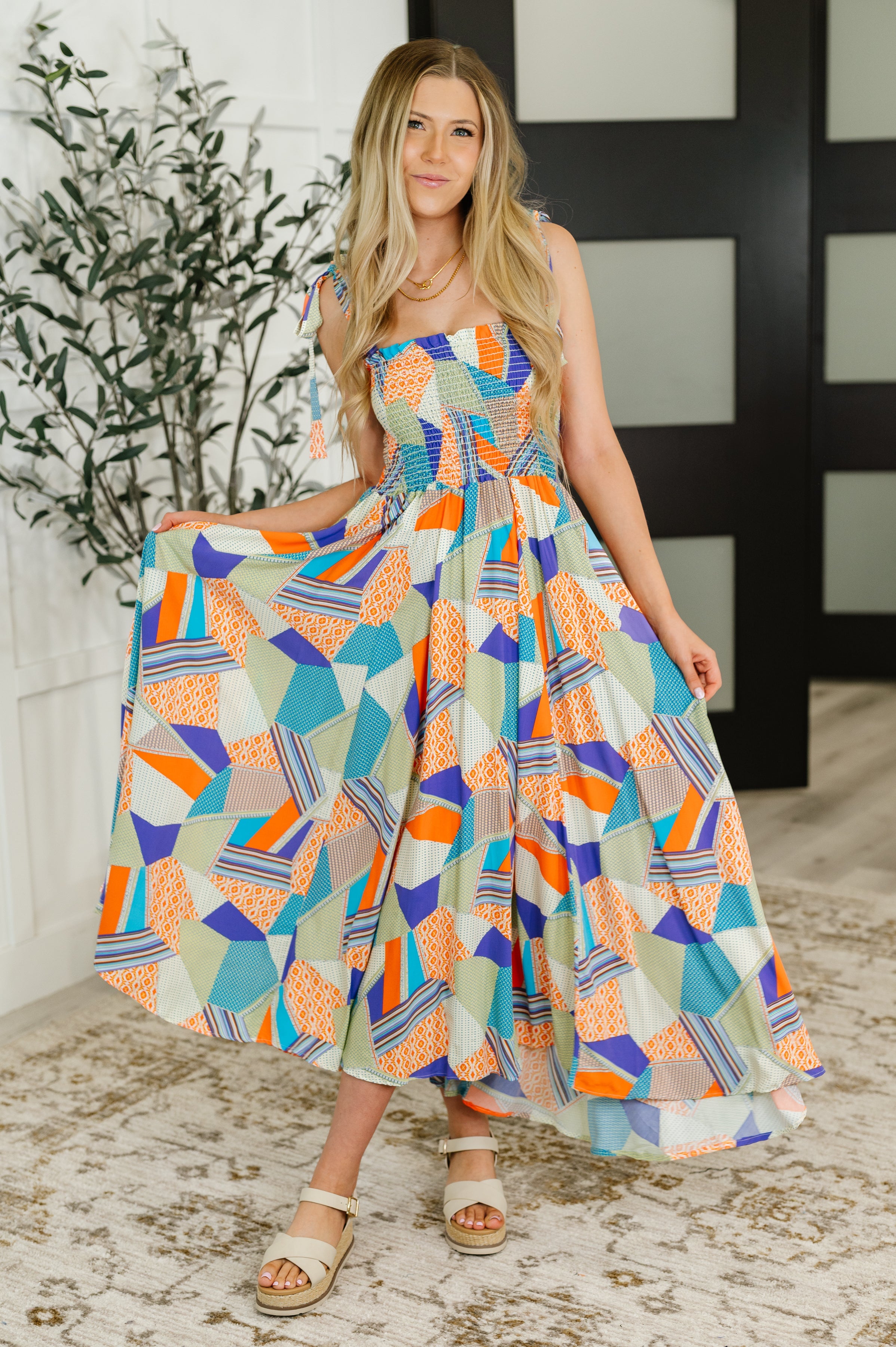 Woman wearing a vibrant patchwork patterned square neck dress with tie straps and beige sandals indoors