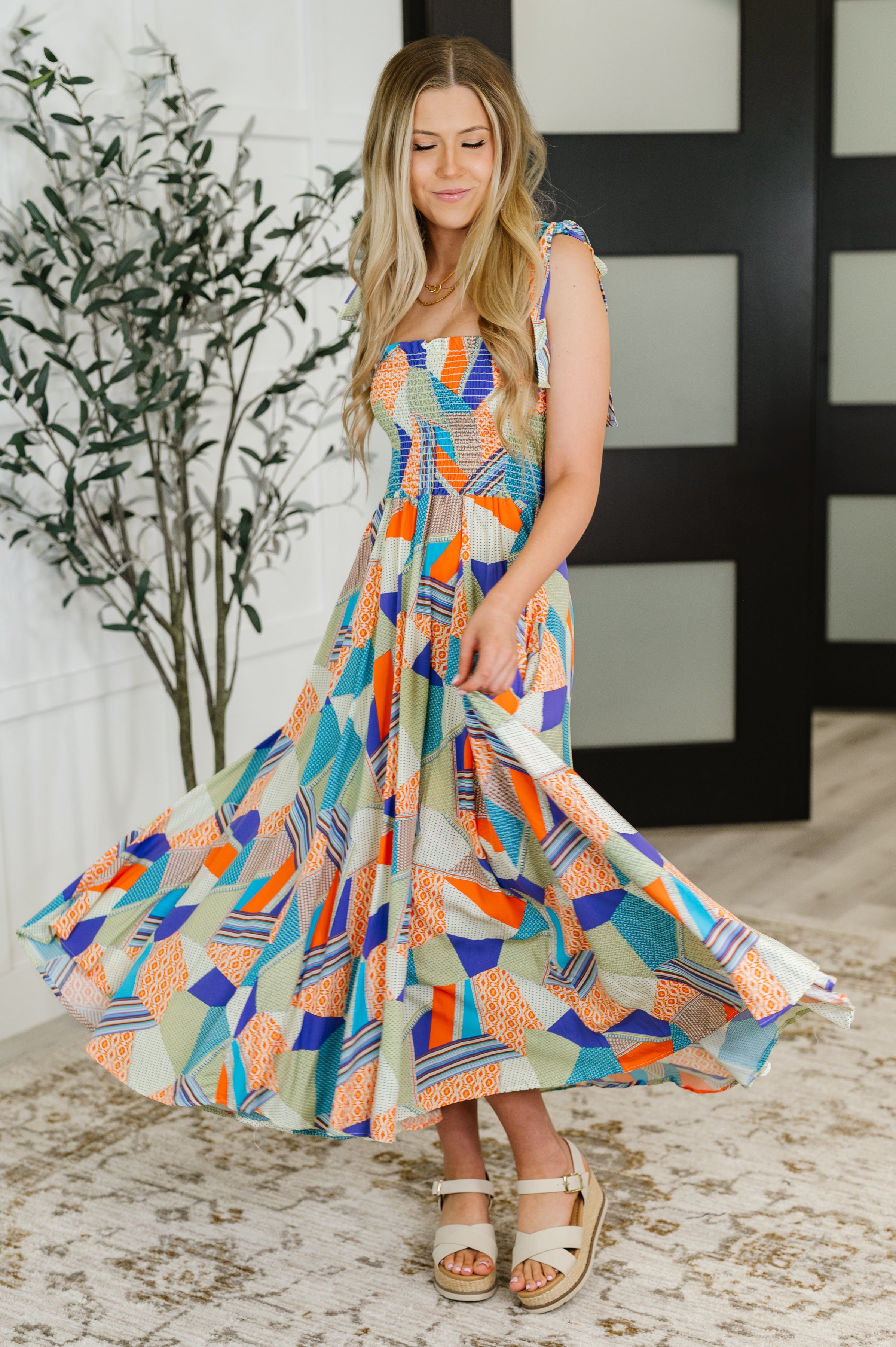 Woman twirling in a vibrant lime, blue, and tangerine patchwork square neck dress with tie shoulder straps indoors